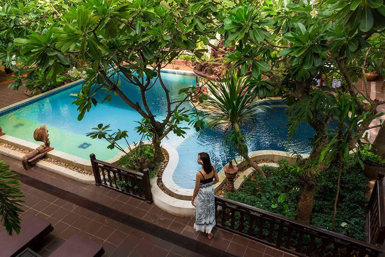 A woman relaxing by a serene boutique resort pool surrounded by tropical palm trees in Cambodia.