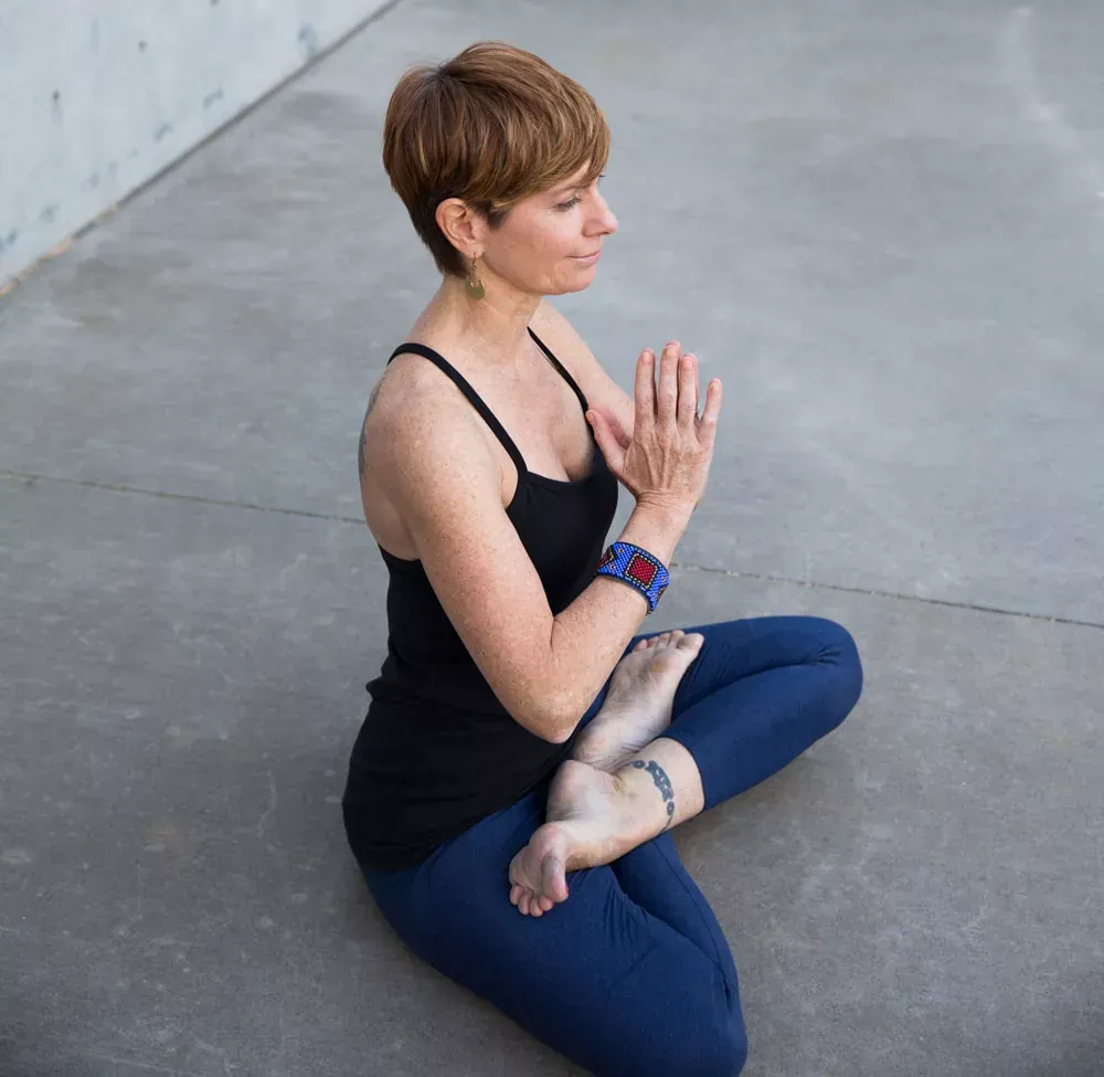 Instructor pressing palms together at the heart in Anjali Mudra to show Namaste at Uptown Yoga.