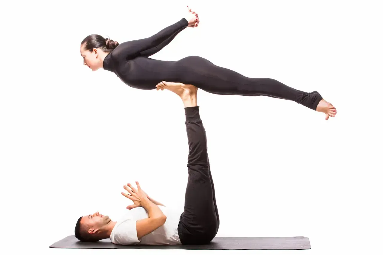 Two partners practicing an acro yoga pose with a base and flyer to build strength at Uptown Yoga in Dallas.