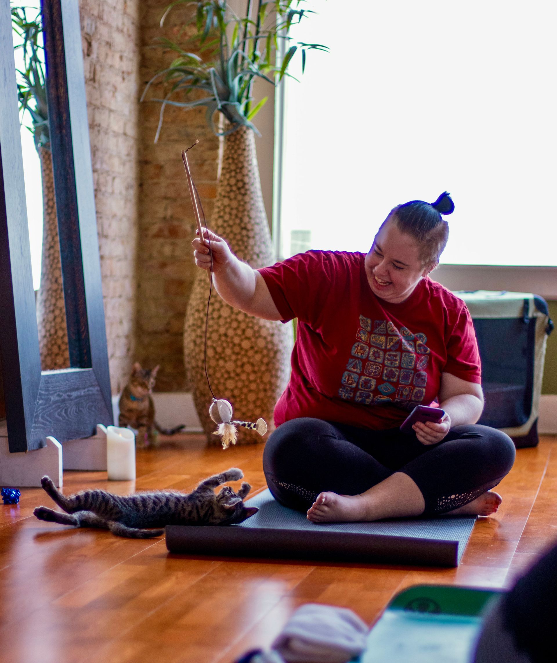 An Uptown Yoga student laughing and playing with a foster kitten rolling on its back using a feather wand toy during a donation-based event for Spicy Whiskers Rescue.