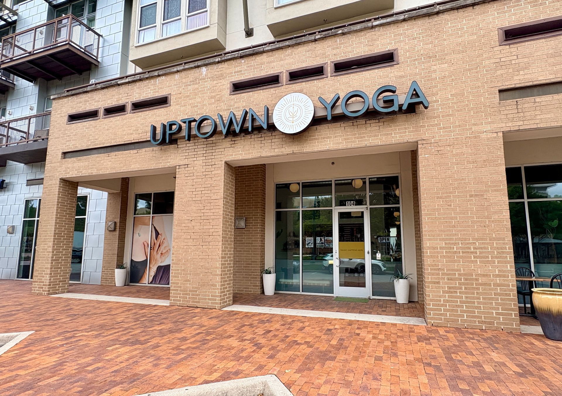 Exterior storefront of the Uptown Yoga Austin Ranch location, featuring a brick facade, large glass windows, and the main entrance sign.