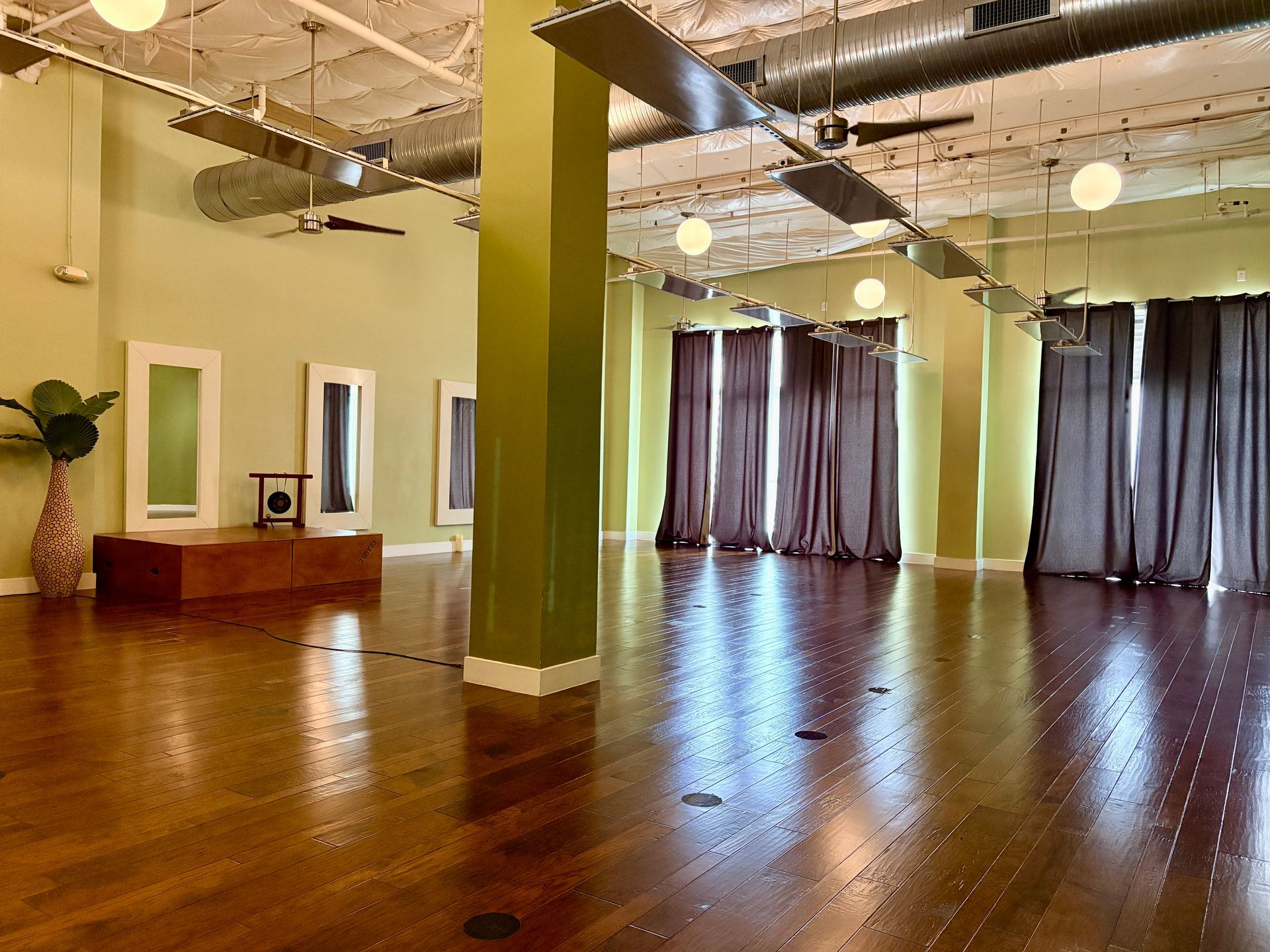 The spacious yoga studio at the Austin Ranch location, featuring hardwood floors, large mirrors, a gong, and ceiling panels for heated yoga classes.
