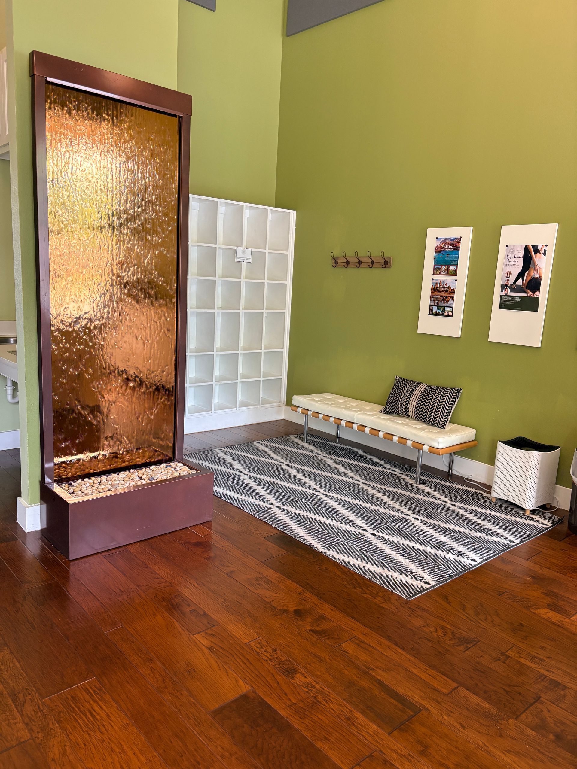 A relaxing waiting area inside the Uptown Yoga Austin Ranch studio, featuring a copper indoor waterfall feature, a modern bench, and student storage cubbies.