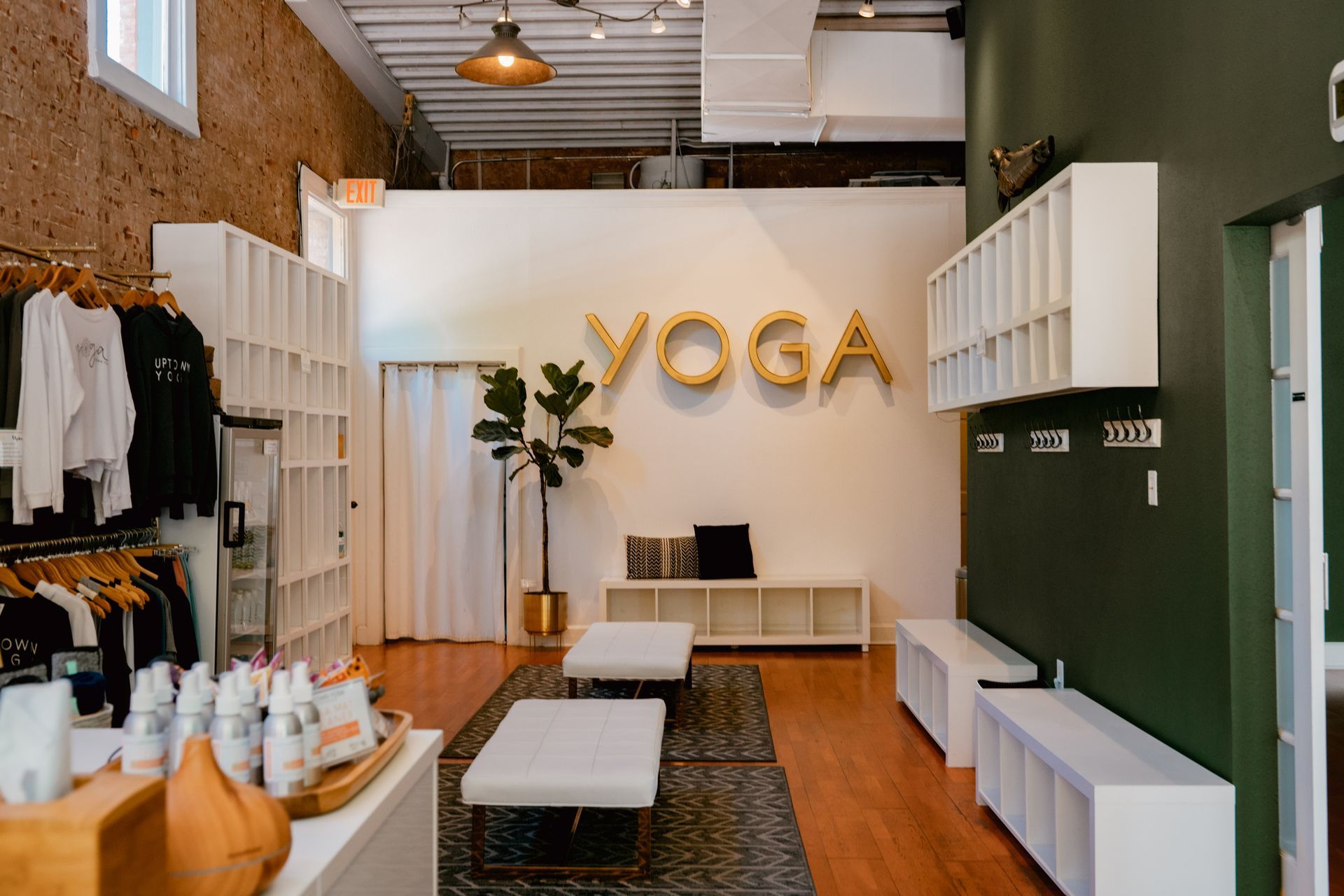 The welcoming lobby and retail boutique at Uptown Yoga Dallas, featuring branded apparel, student storage cubbies, modern white seating, and large gold lettering spelling 'YOGA'.