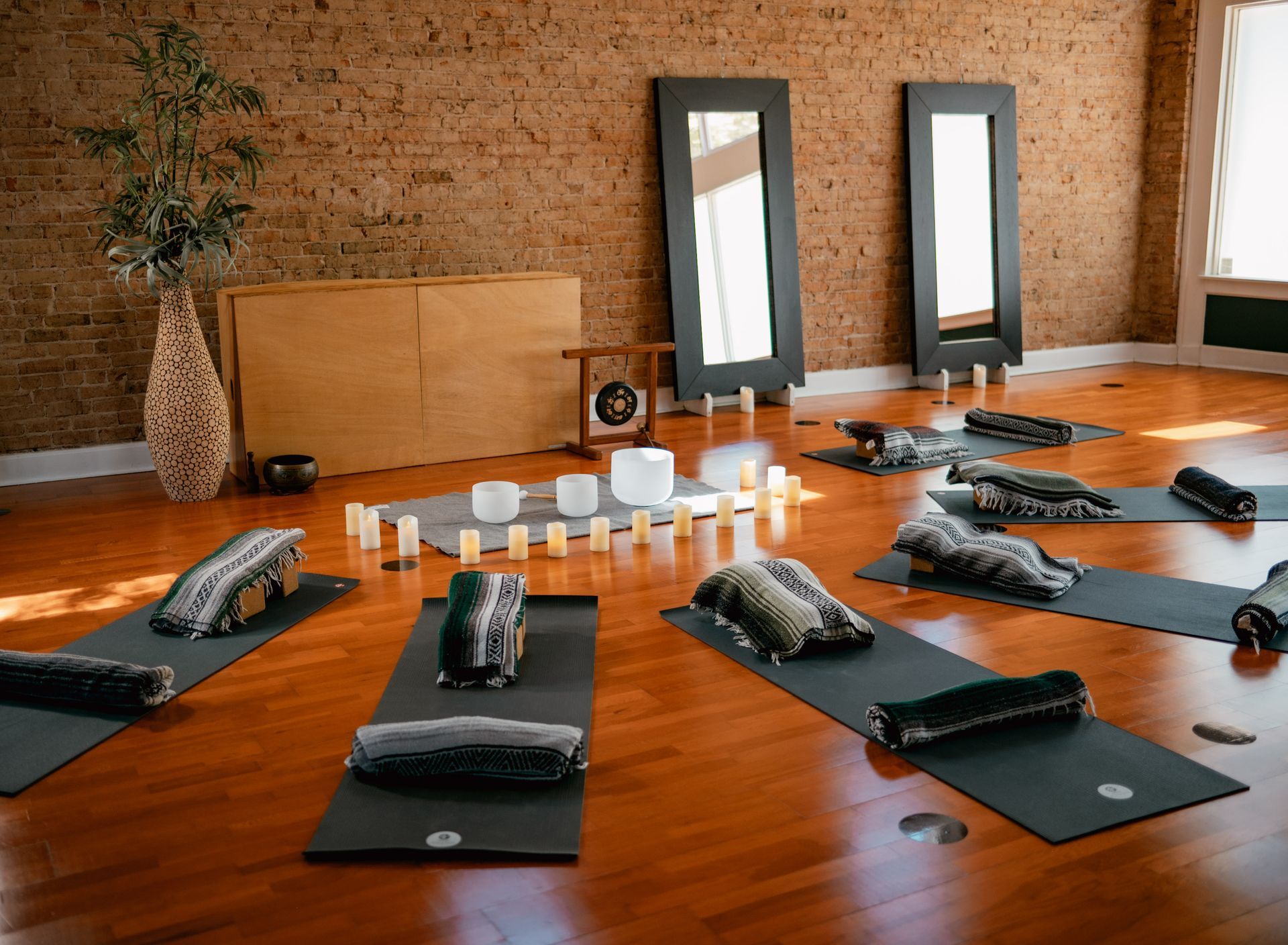 Yoga studio set up for a sound healing and restorative class at Uptown Yoga Dallas, featuring mats, folded blankets, crystal singing bowls, and exposed brick walls.