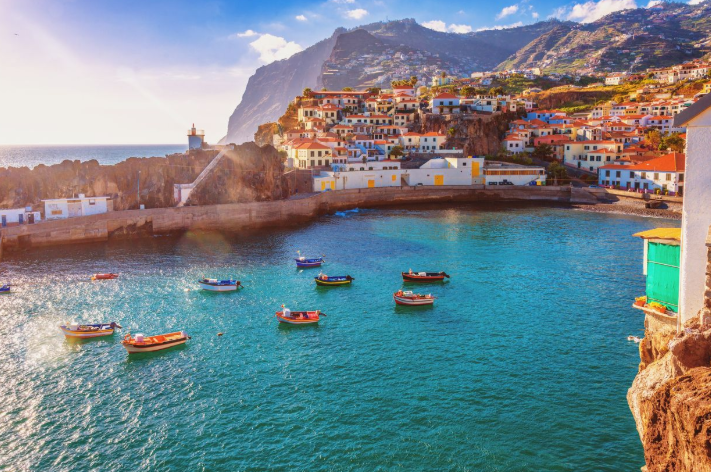 Scenic coastal view of Madeira, Portugal, featuring colorful boats and volcanic mountains for Uptown Yoga's island movement and mountain retreat.