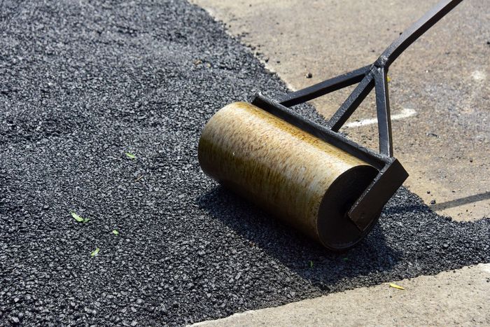 A road roller compressing fresh asphalt on a newly paved surface.