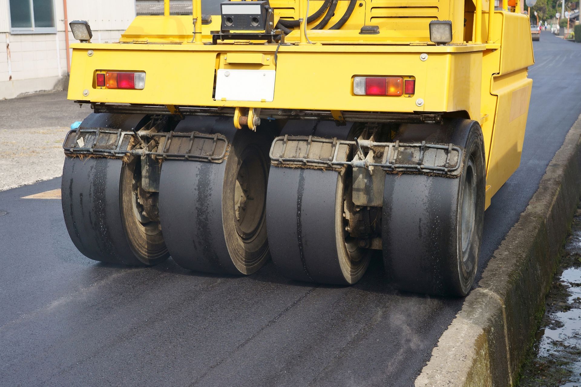 A yellow truck is rolling asphalt on a road