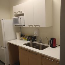 A kitchen with a sink , refrigerator , microwave , and kettle.
