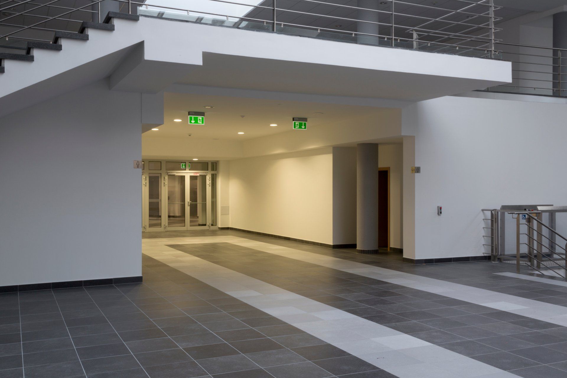 An empty hallway with stairs and a green exit sign