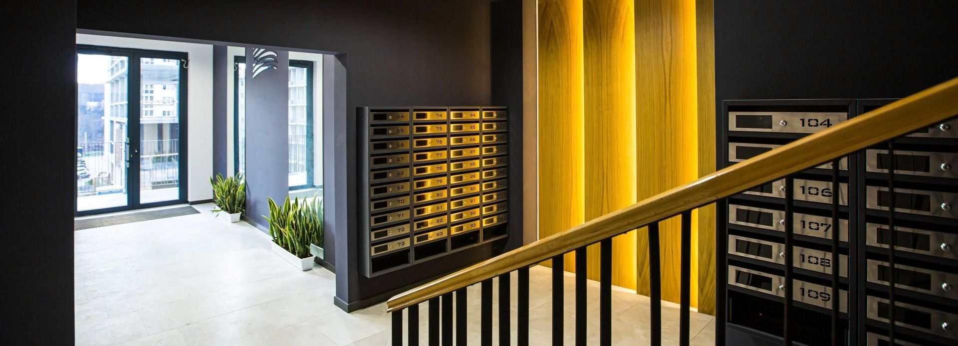 A modern apartment building hallway with mailboxes, stairs, and a door to the outside.