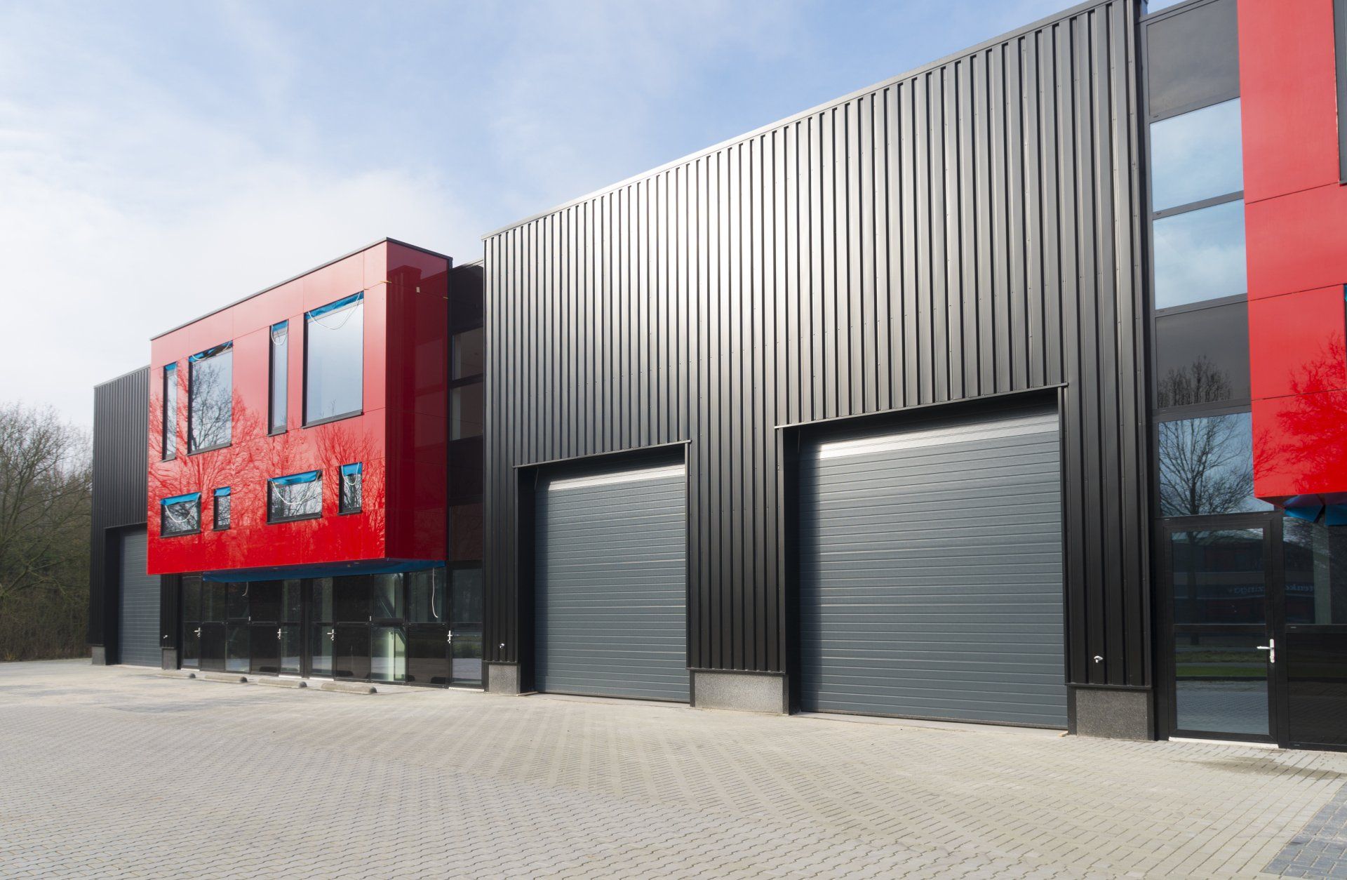 Modern warehouse exterior with red accents, black corrugated metal walls, and two gray roll-up doors on a paved lot.