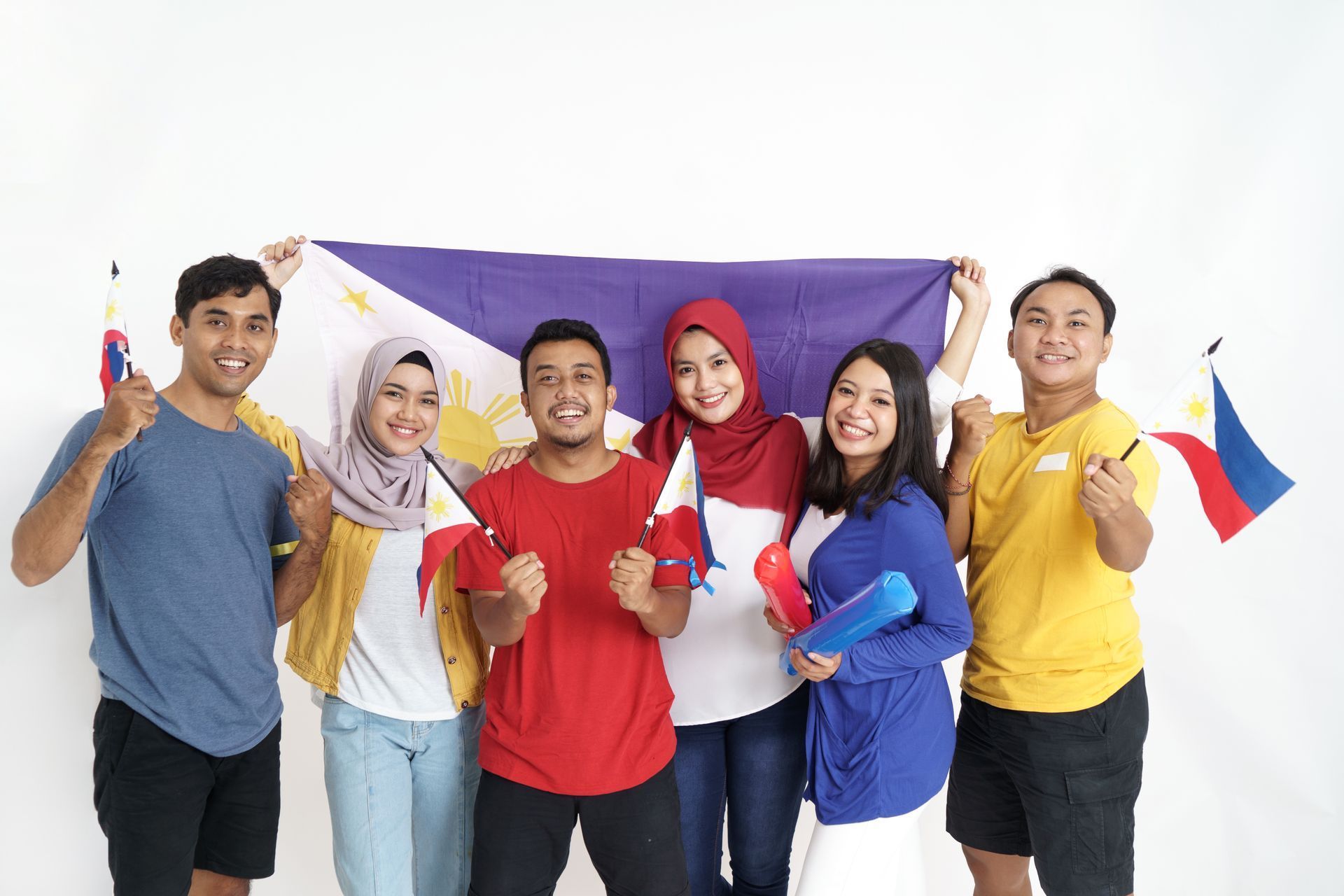 Group of people smiling, holding Philippine flags, and a large flag in front of a white background.