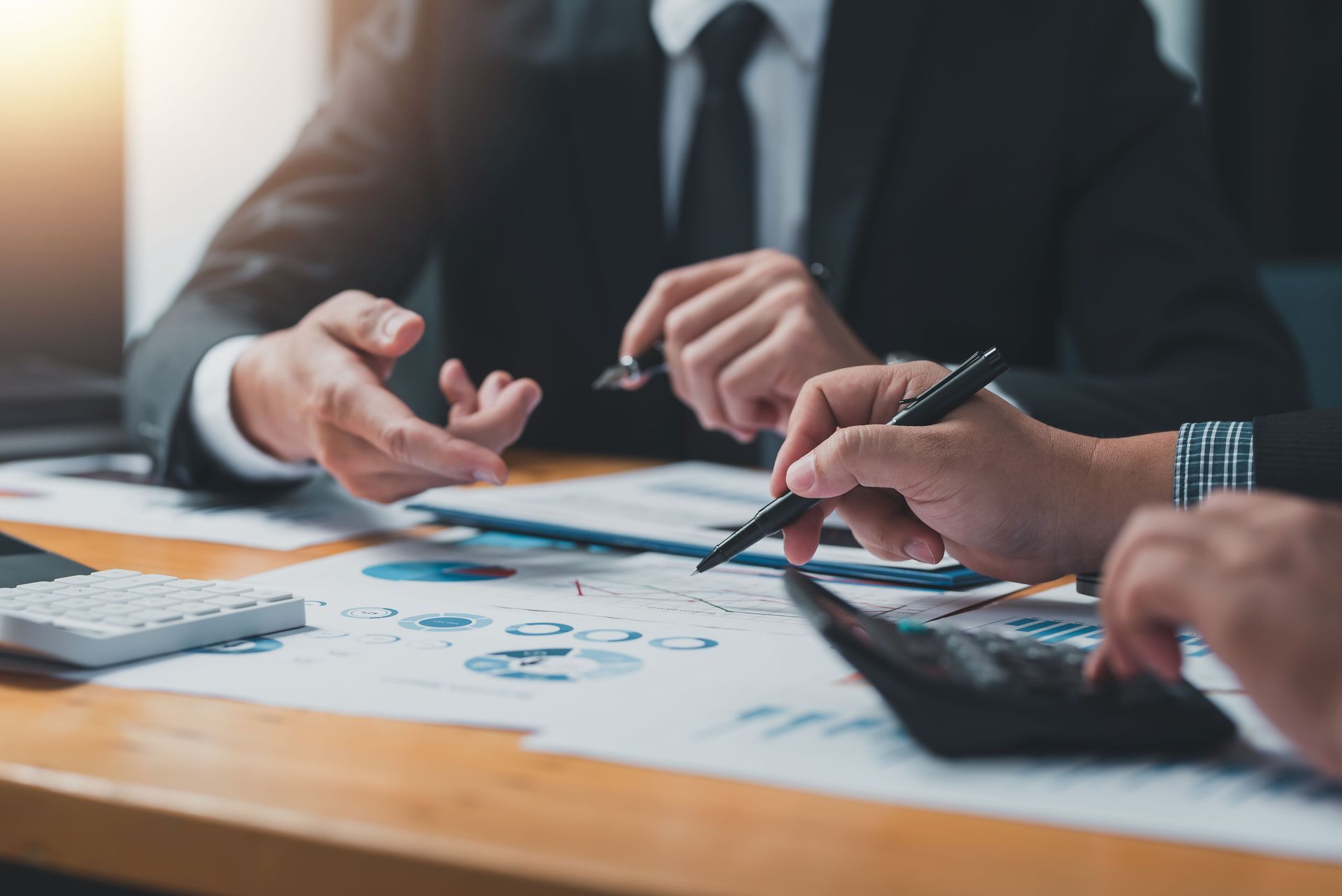 Two businesspeople in suits reviewing financial charts and using a calculator at a table.