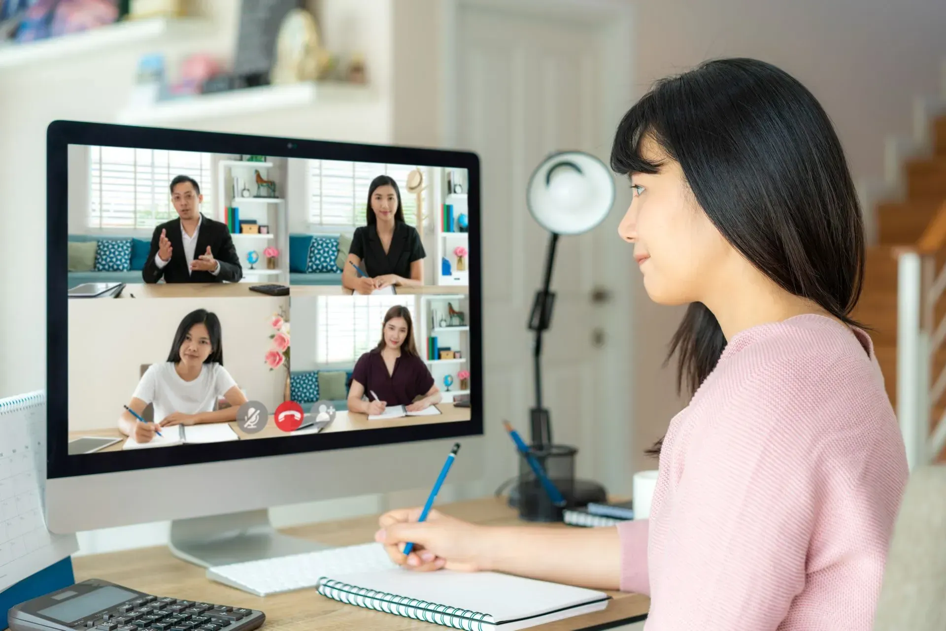 Woman at desk, attending a video conference on a computer; taking notes.