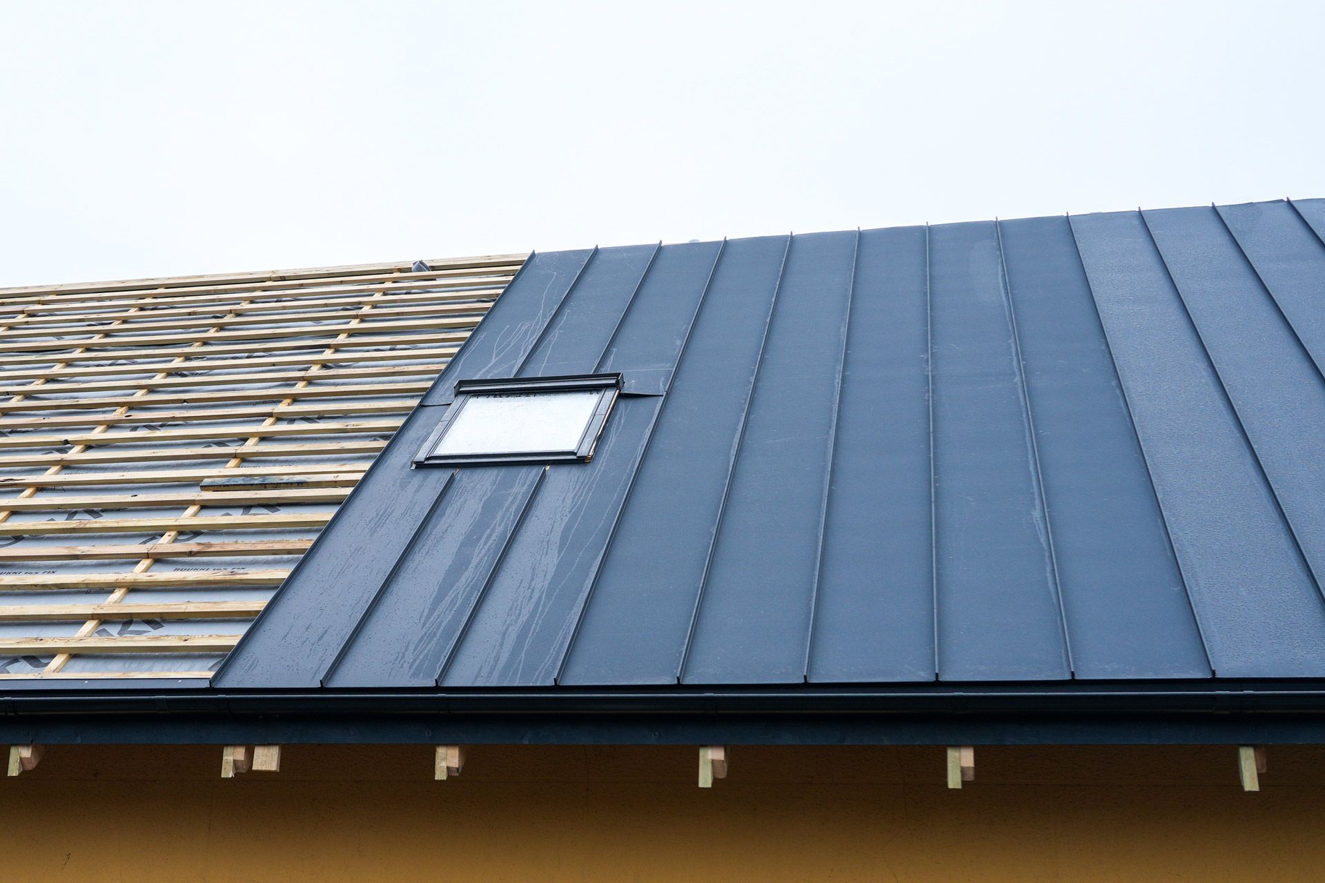 A roof partially covered in dark metal sheeting, with exposed wooden beams and a skylight.
