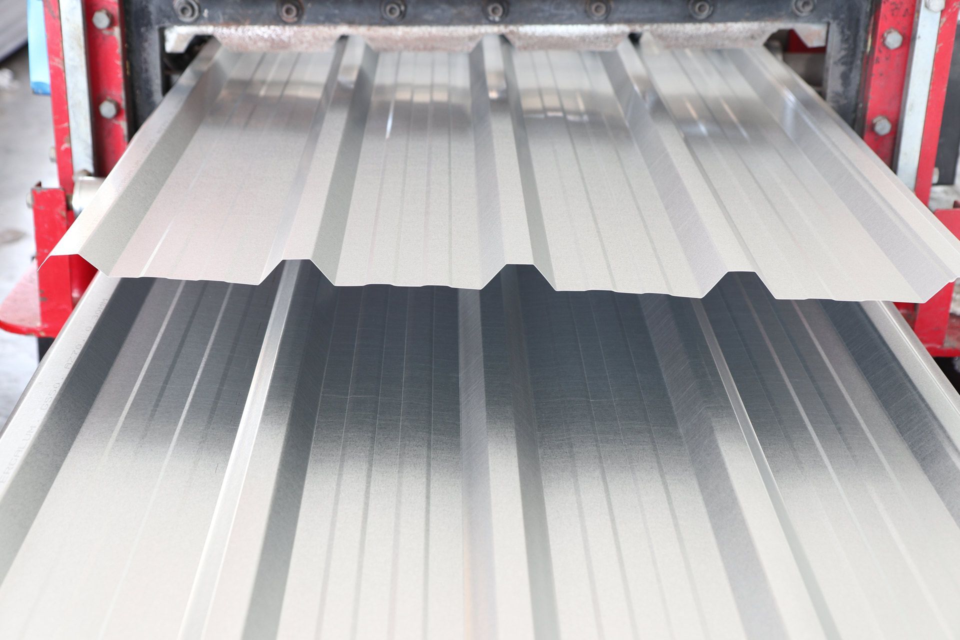 Metal roofing sheets being formed by a machine, in a factory setting.