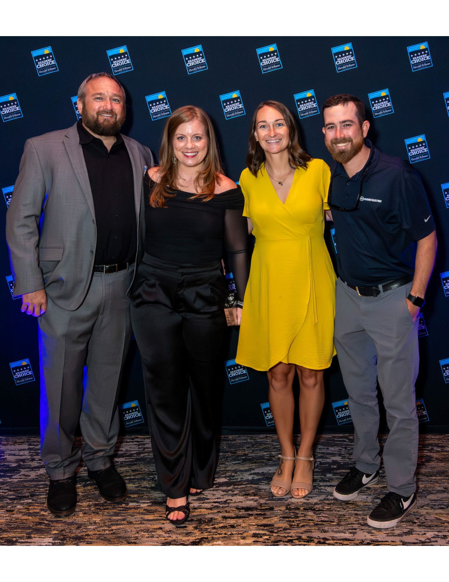 Four people pose for a photo in front of a blue branded backdrop at the Sarasota Community Choice Awards