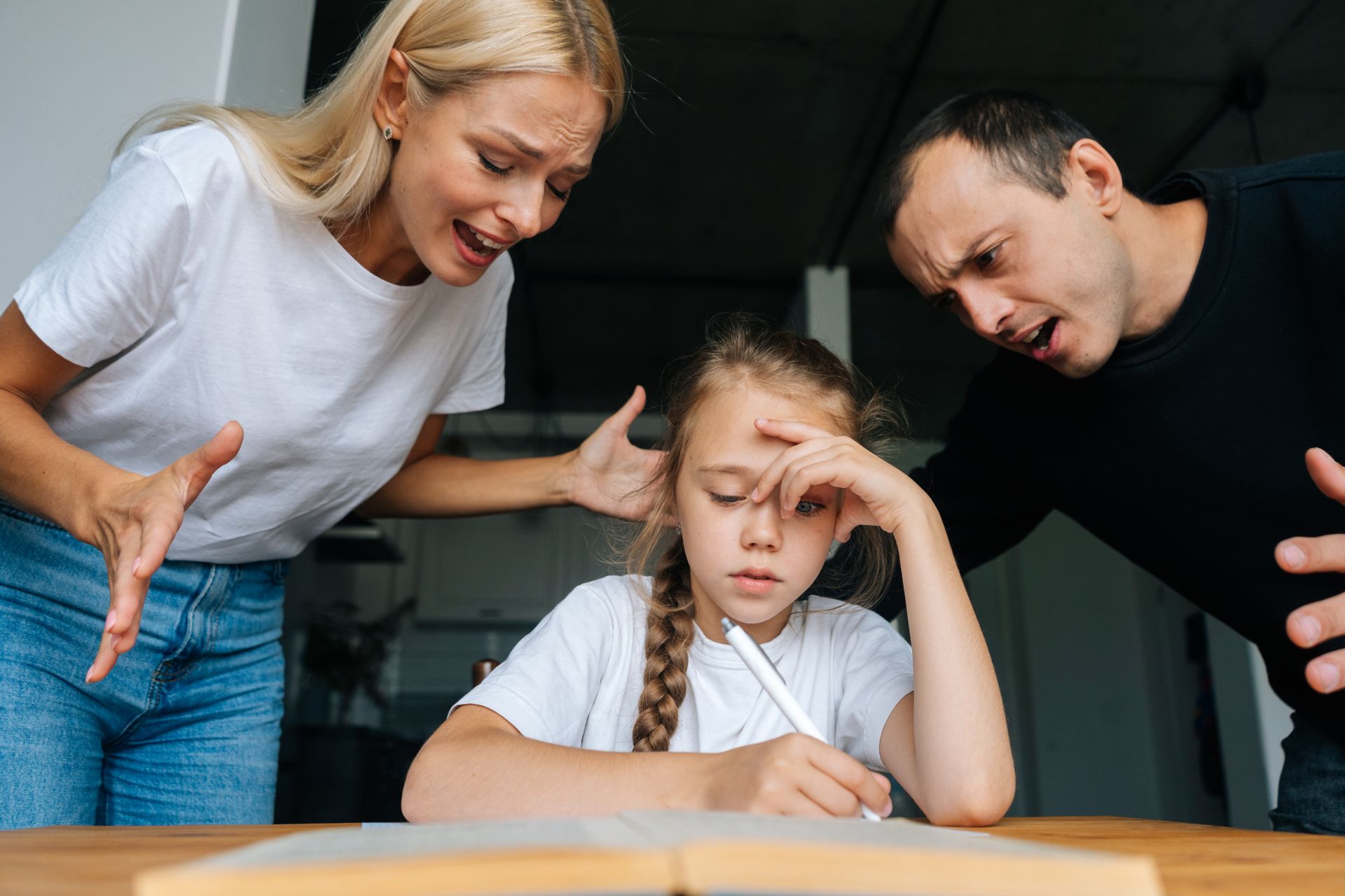 Genitori che urlano a un bambino, che sta scrivendo a un tavolo, apparendo stressato.