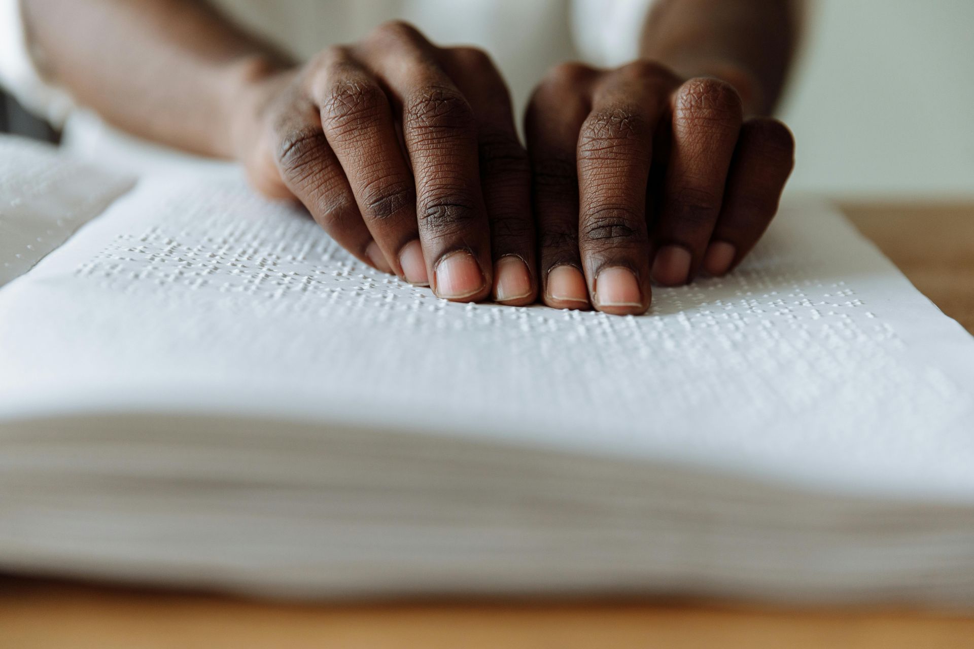 Mani di una persona con pelle scura che leggono il Braille su una pagina bianca.