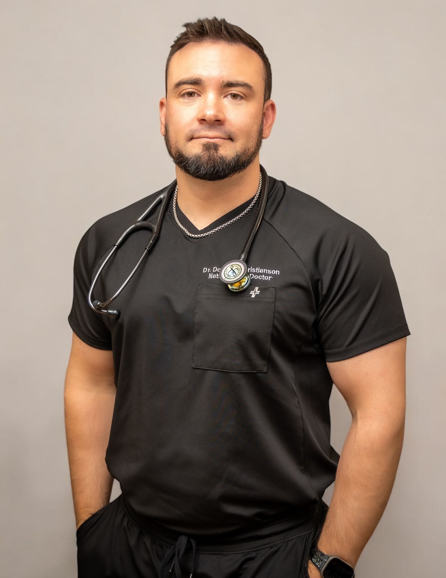 A person in a black shirt with a stethoscope, standing against a plain background.