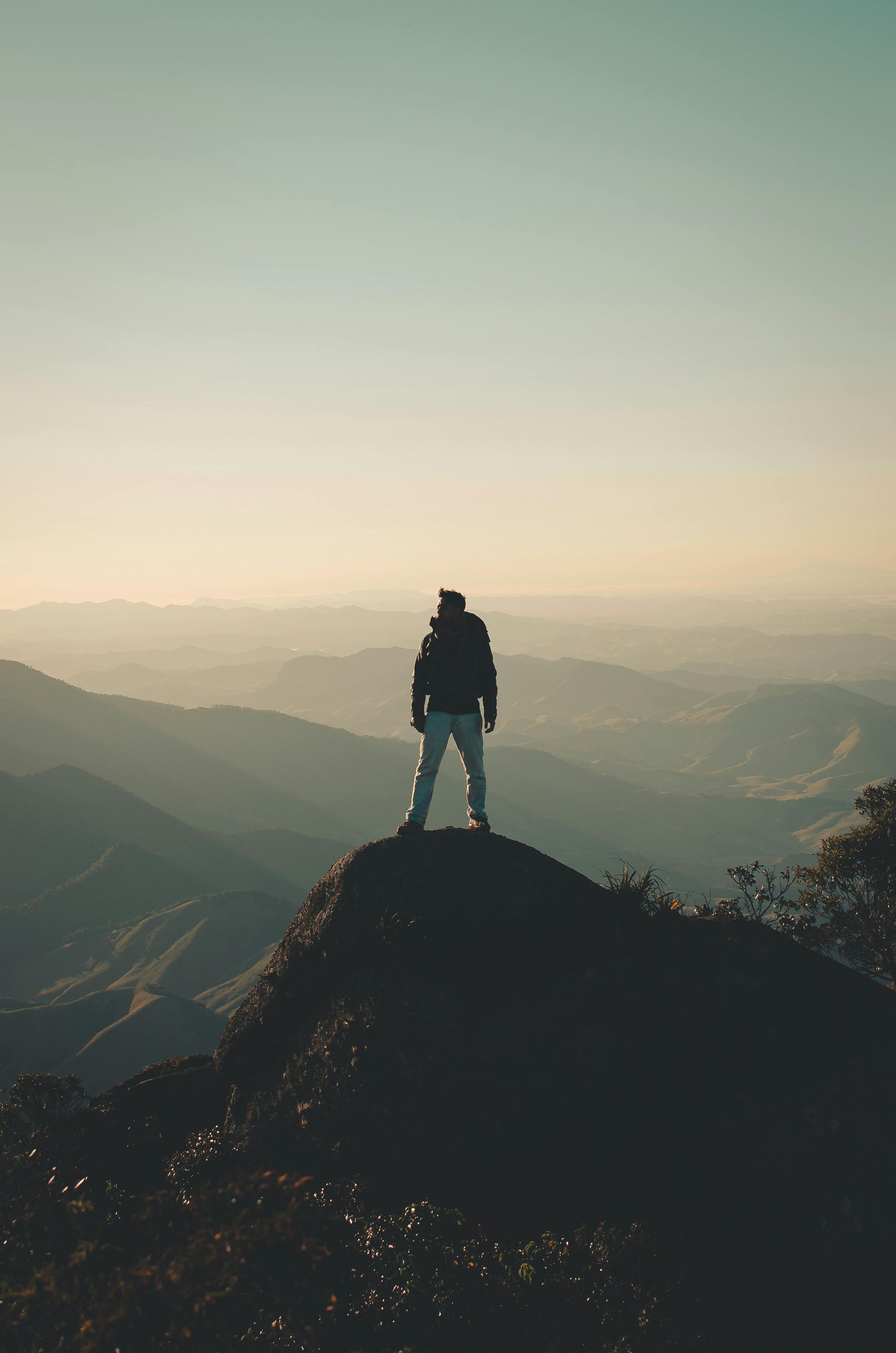 Person standing on a mountain peak at sunrise, overlooking a misty valley.