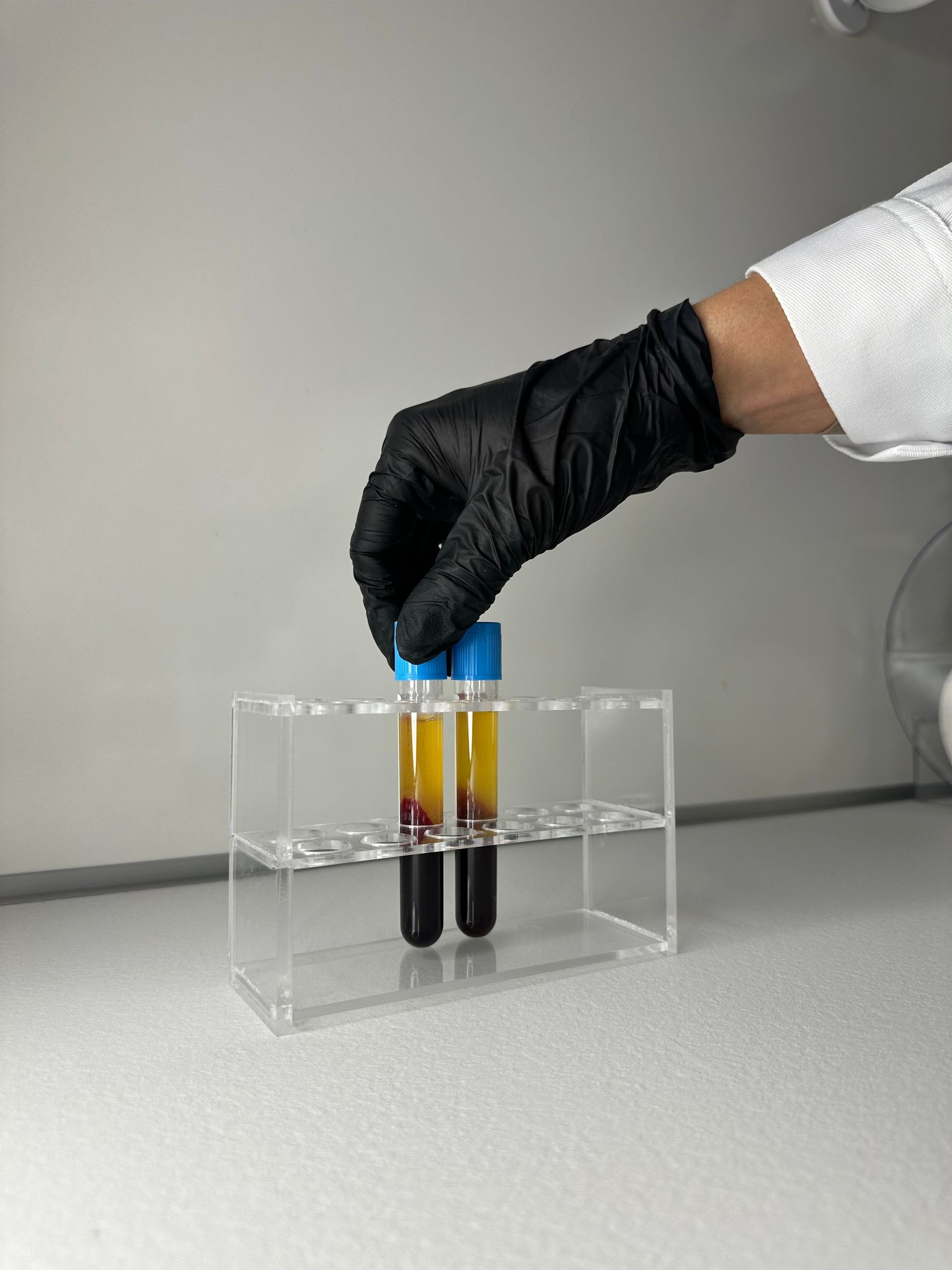 Gloved hand holding test tubes with dark liquid in a clear lab rack