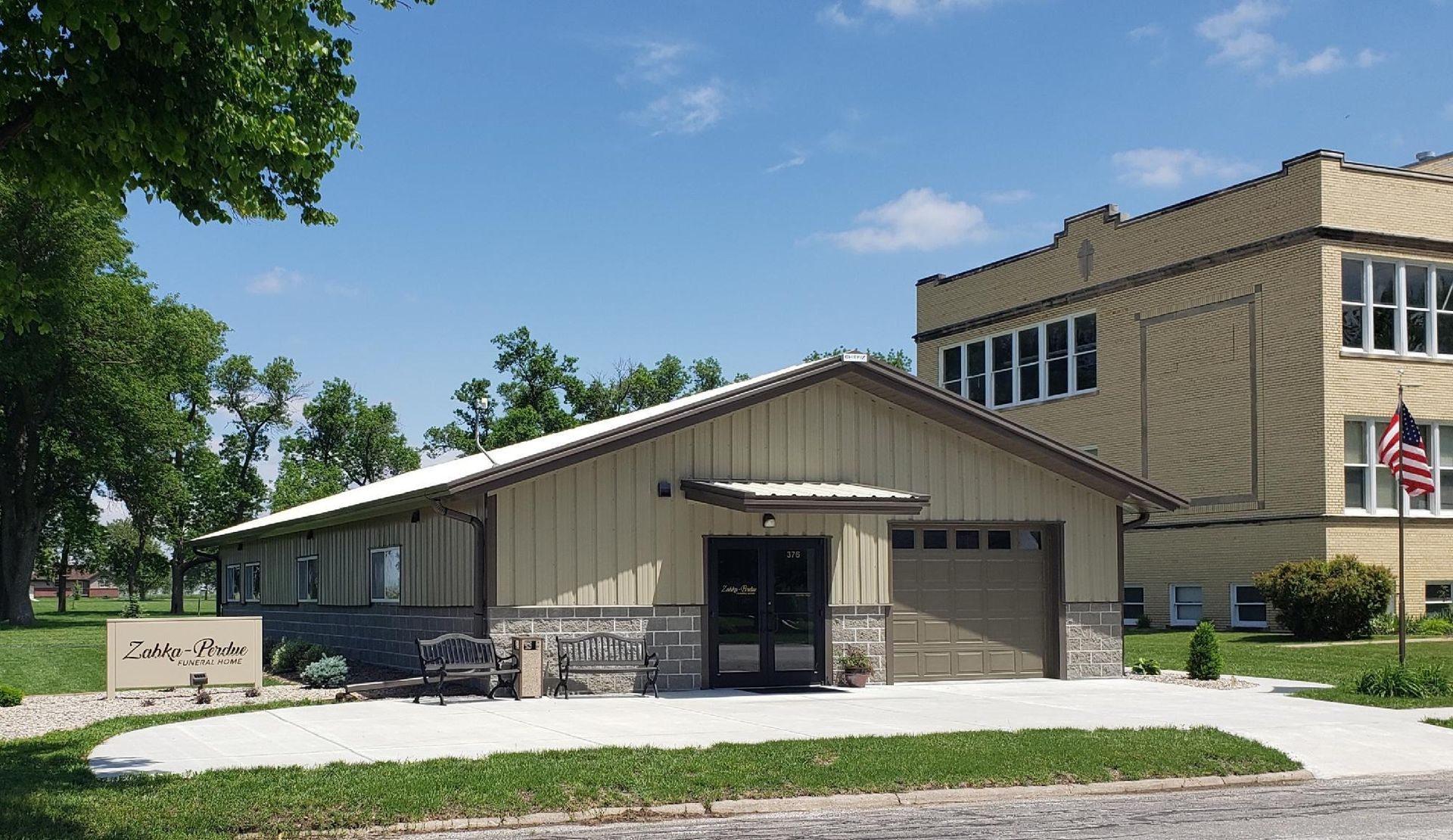 A light tan building with a garage door and stone accents in front of an older building under a blue sky.