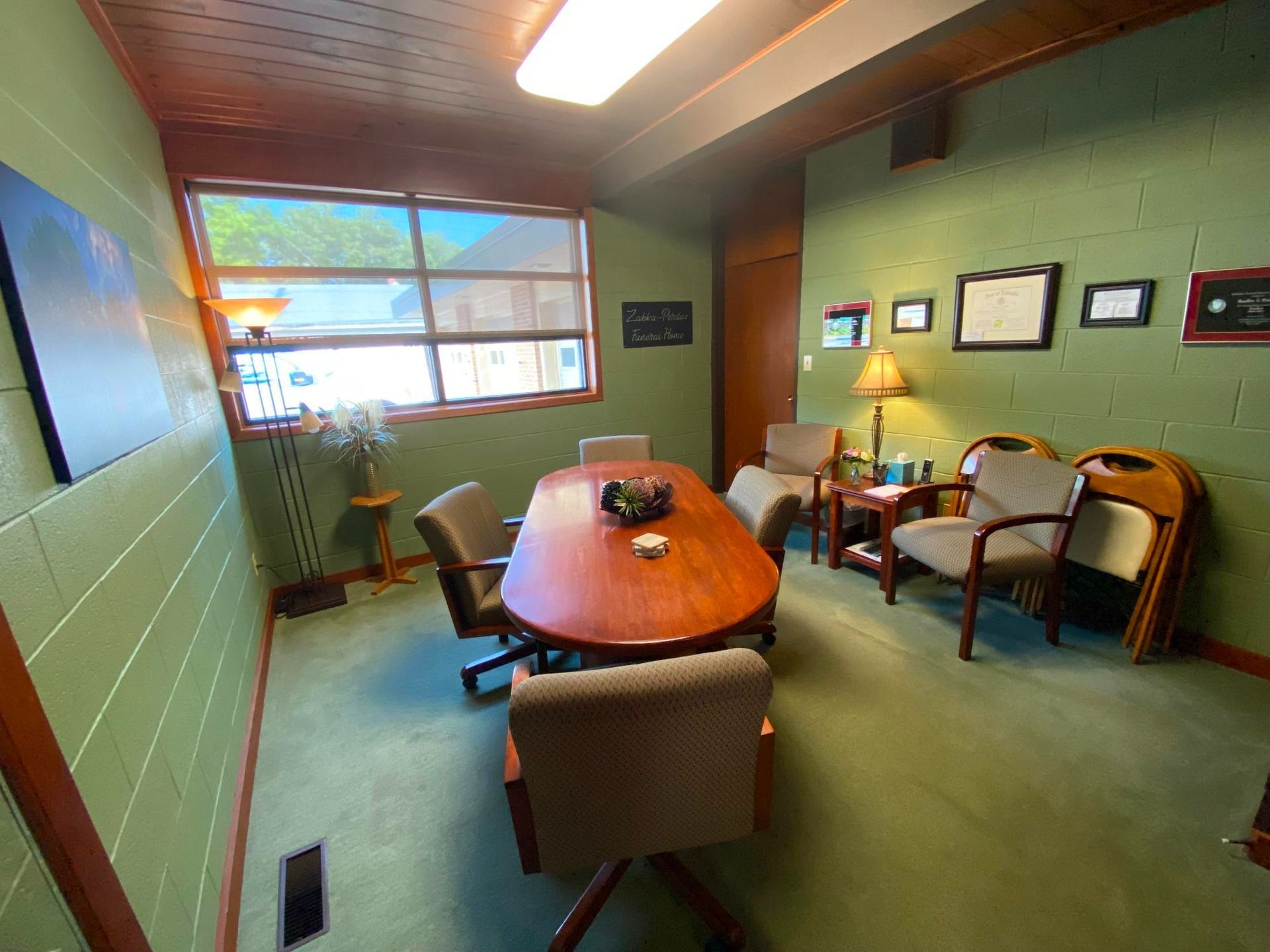 Conference room with oval table, chairs, window, and green walls.