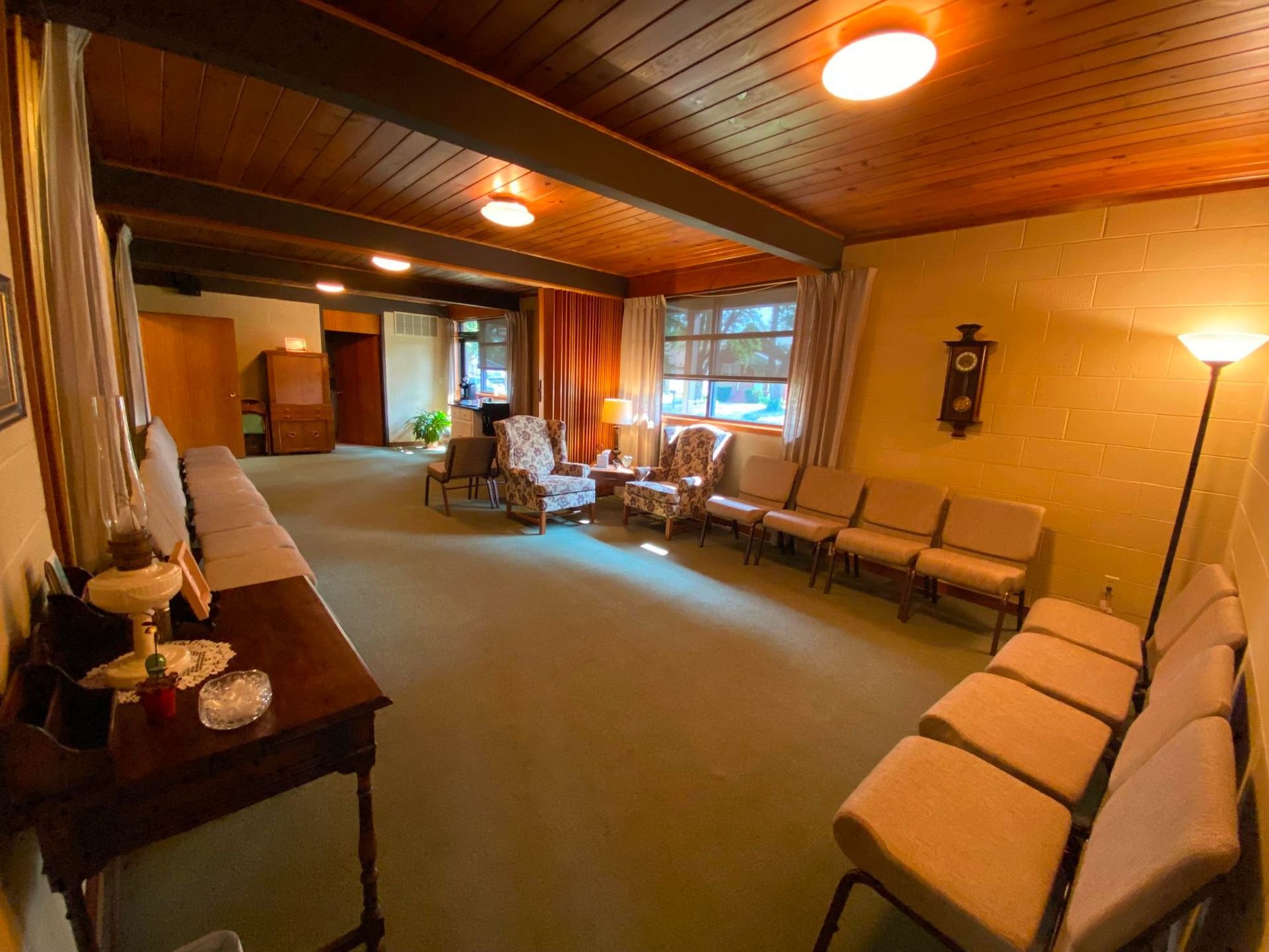 Awaiting room with olive carpet, light tan chairs, wooden ceiling, and antique clock.