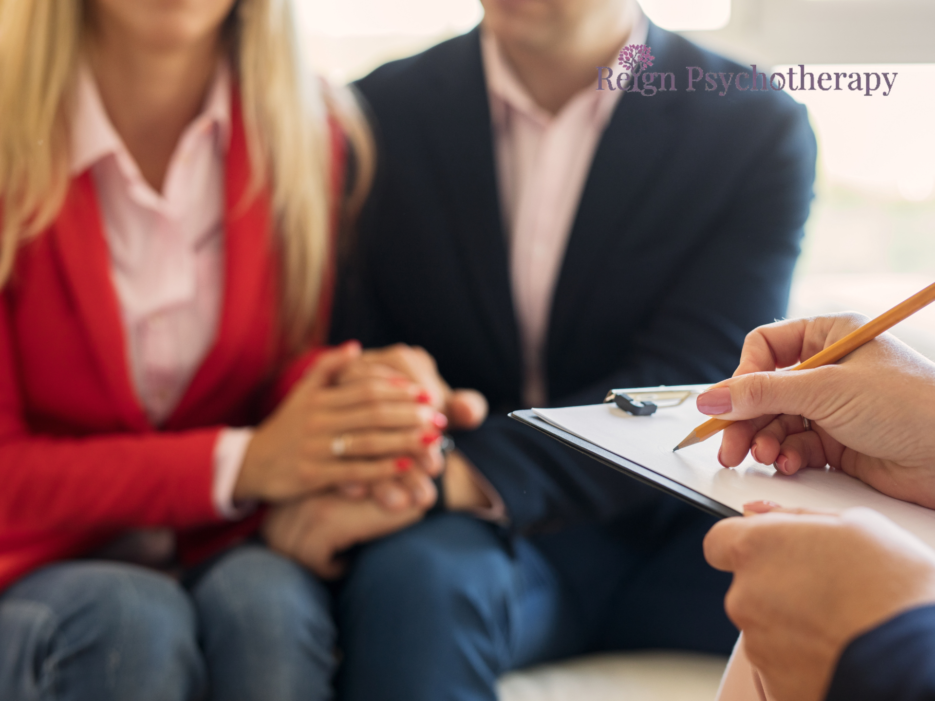 a couple holding hands in a counseling session while a therapist is writing.