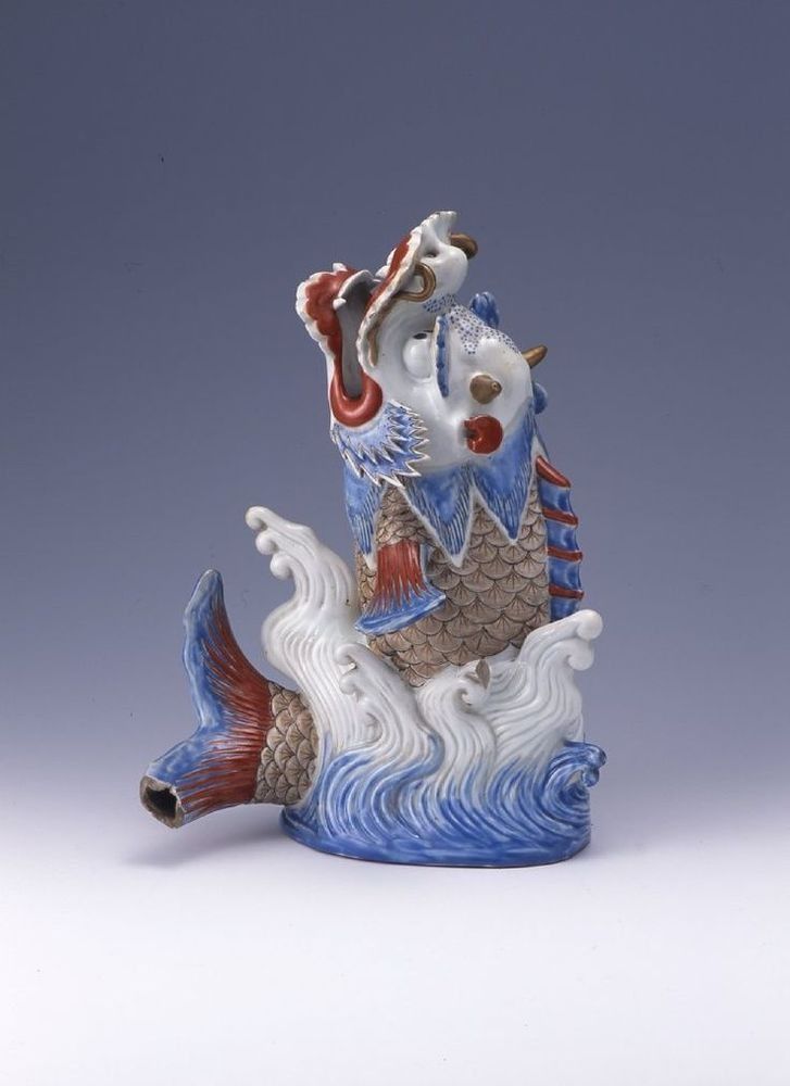 Ceramic carp-dragon emerging from waves, blue and red with open mouth.