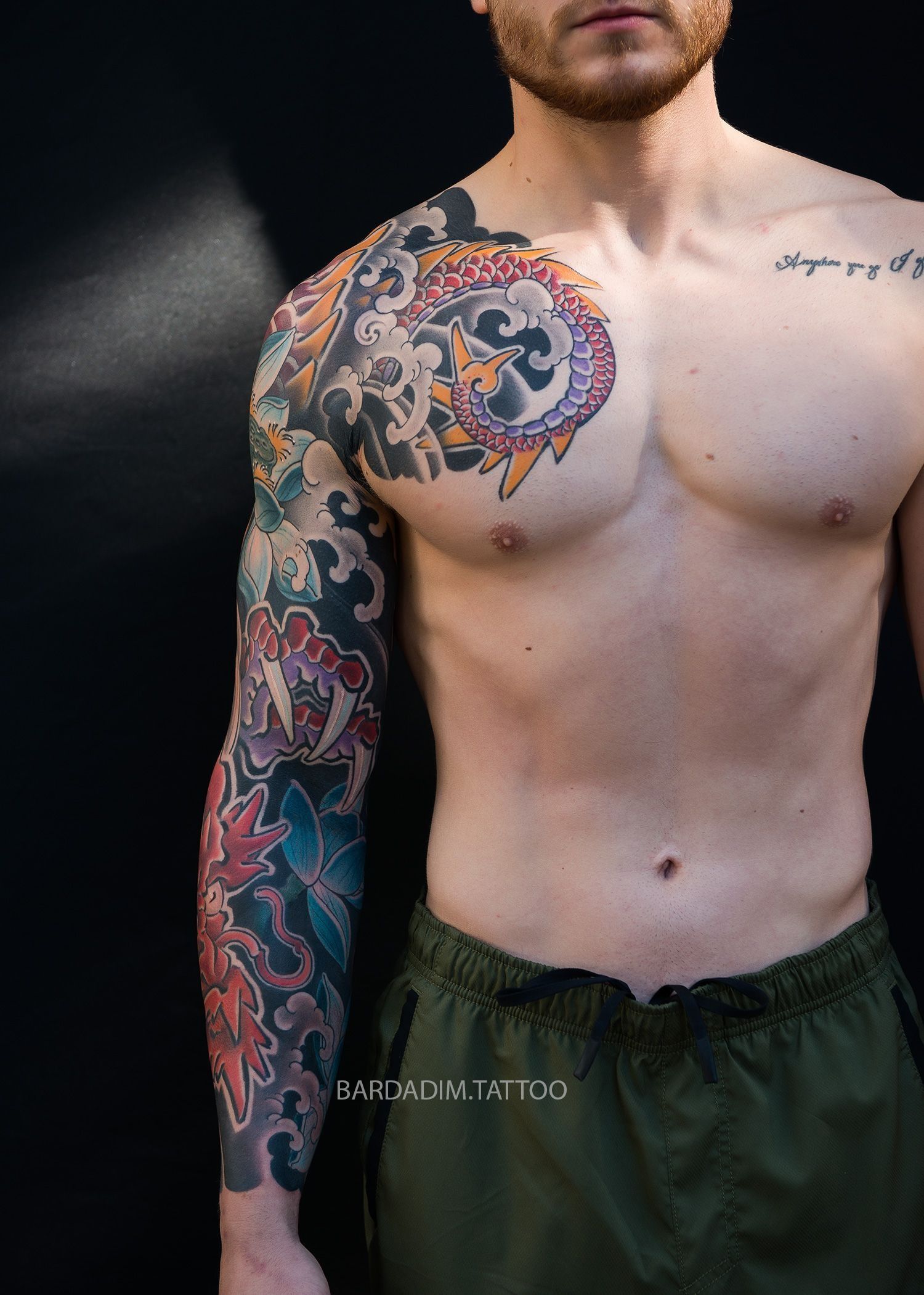 A shirtless man with a colorful tattoo on his arm and chest.