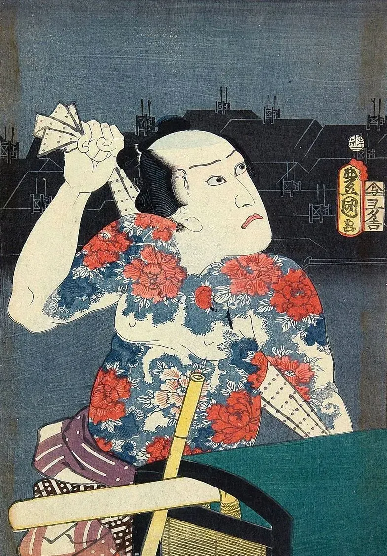 Man with floral tattoos and shaved head, holding a cloth, next to a lamp in a dark setting.