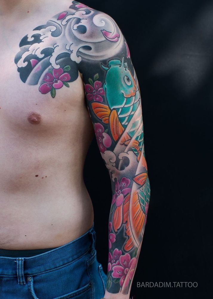 Man's arm tattooed with Japanese koi fish, waves, and flowers in vibrant colors, against a dark background.