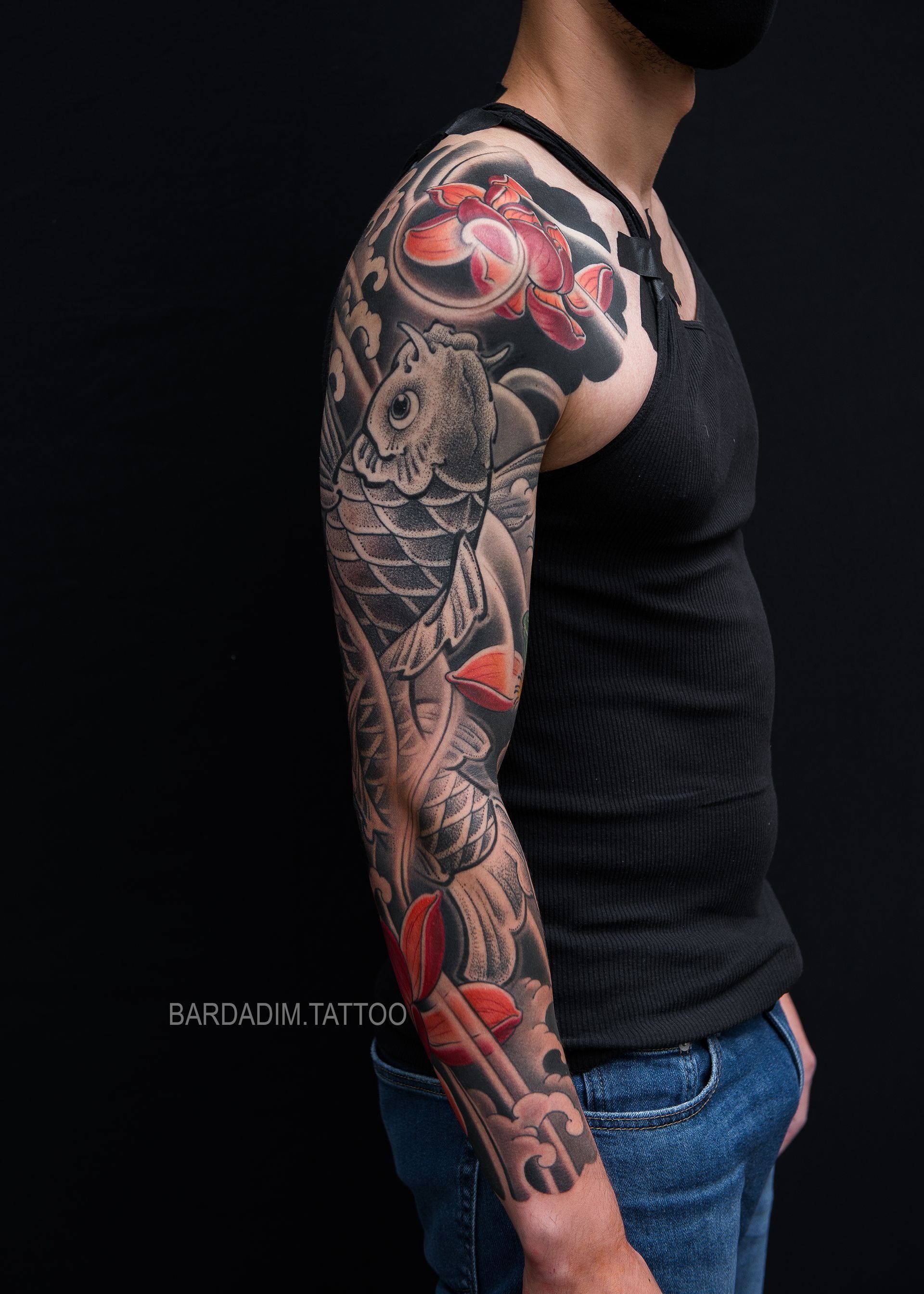 Man with full sleeve Japanese Irezumi tattoo of koi fish, flowers, and water against a black background.