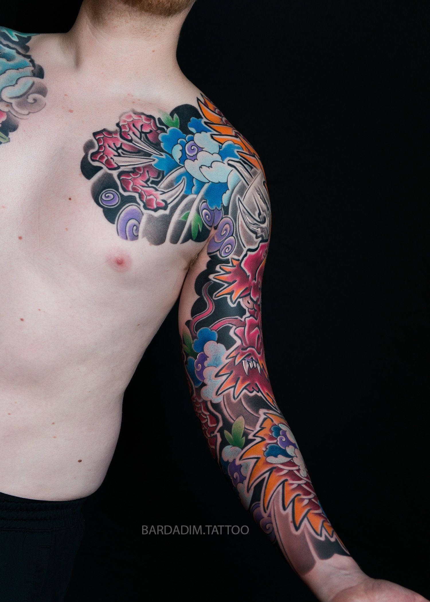 A shirtless man with a colorful tattoo on his chest and arm.