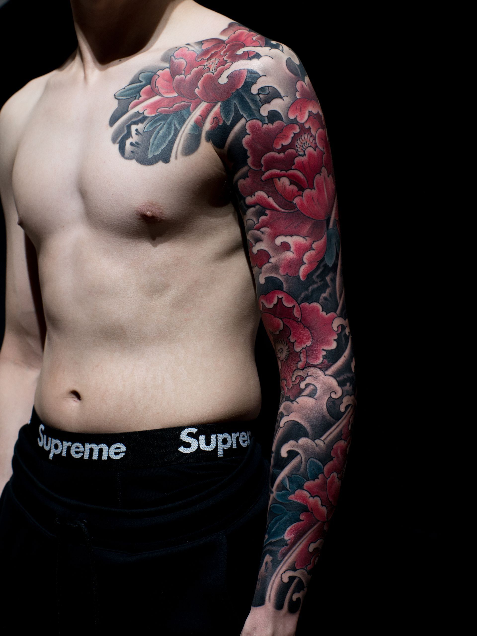 A shirtless man with a full sleeve tattoo wearing supreme underwear