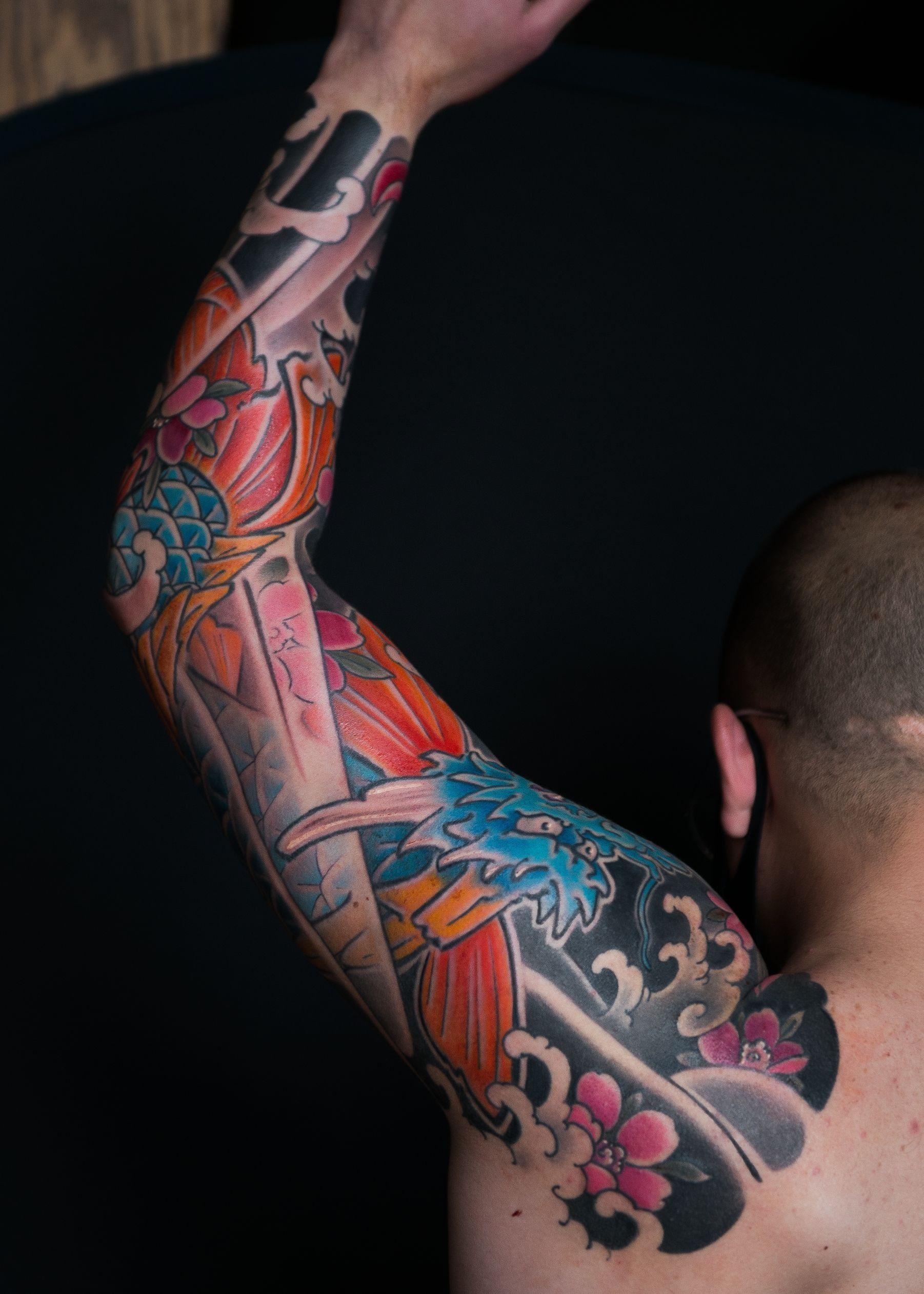Full sleeve tattoo in vibrant colors of a koi-dragon, flowers, and waves at Bardadim Tattoo.
