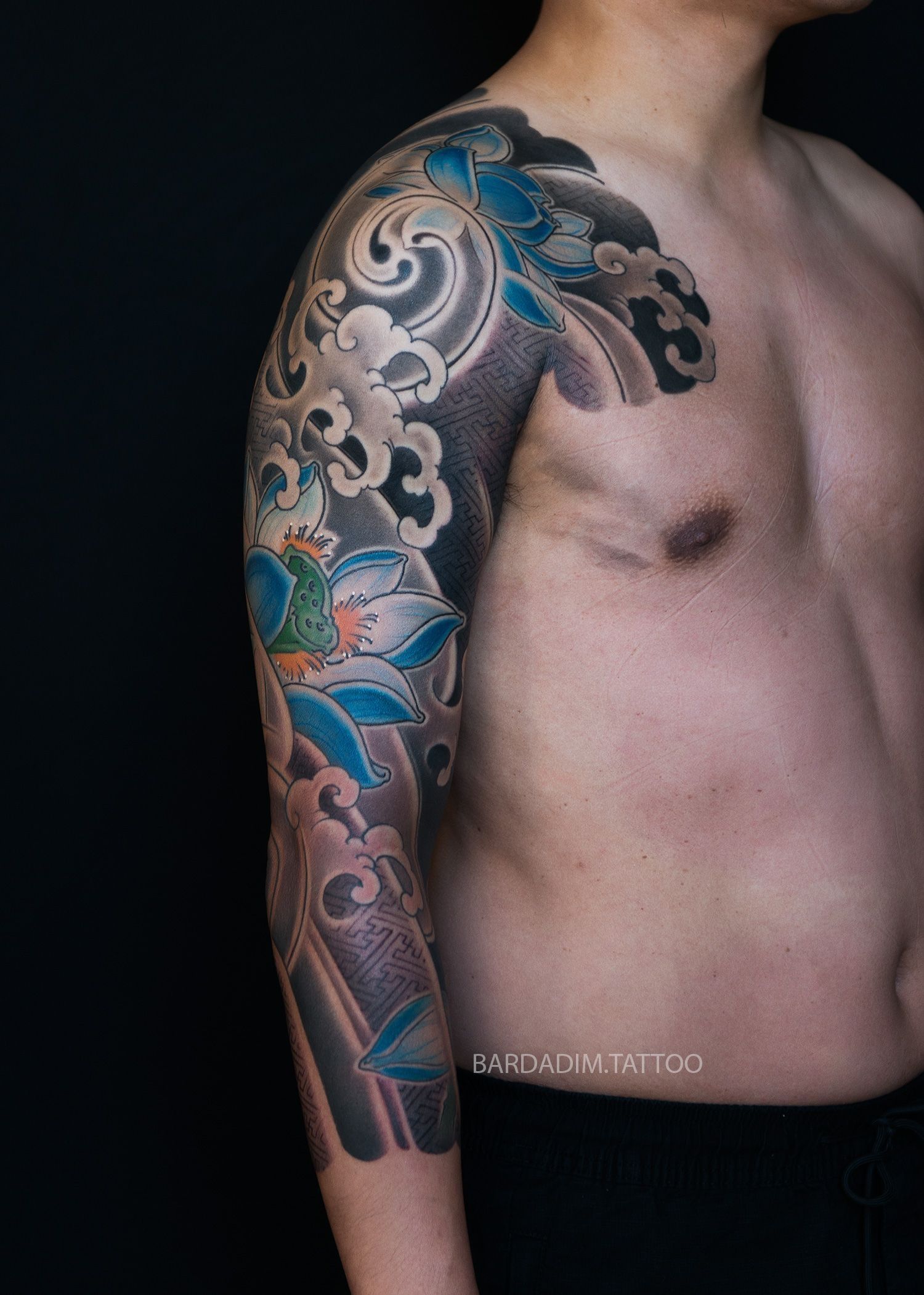 A man without a shirt has a tattoo on his arm and chest.