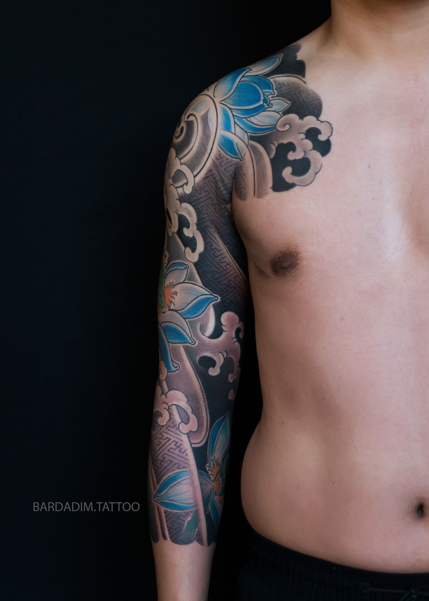 A man without a shirt has a tattoo on his arm and chest.