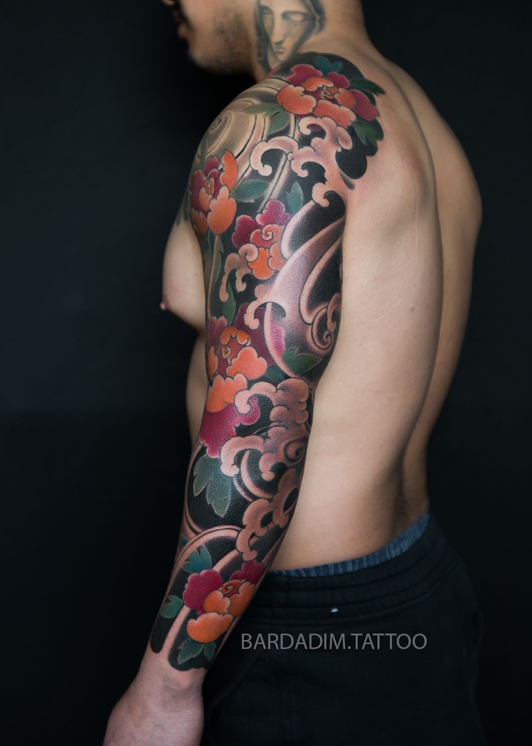 A shirtless man has a full sleeve tattoo of flowers and waves