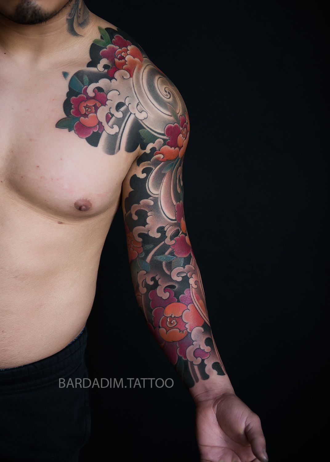 A shirtless man with a tattoo on his arm and chest.