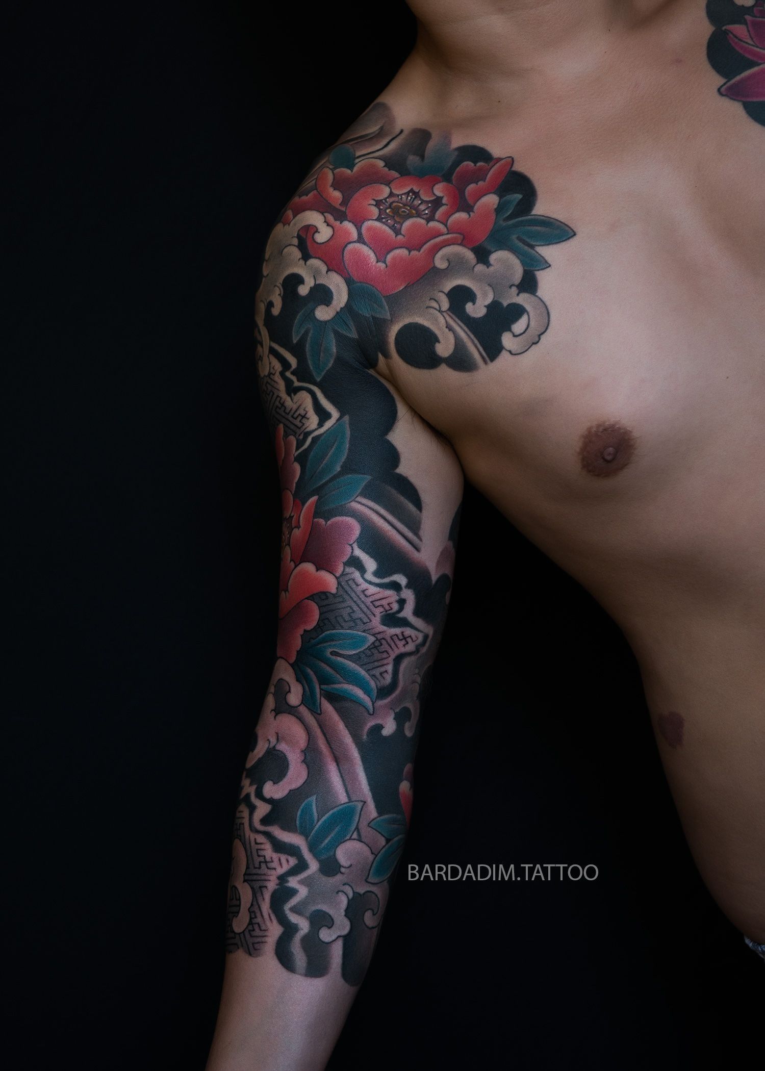 A man without a shirt has a tattoo on his shoulder and chest.