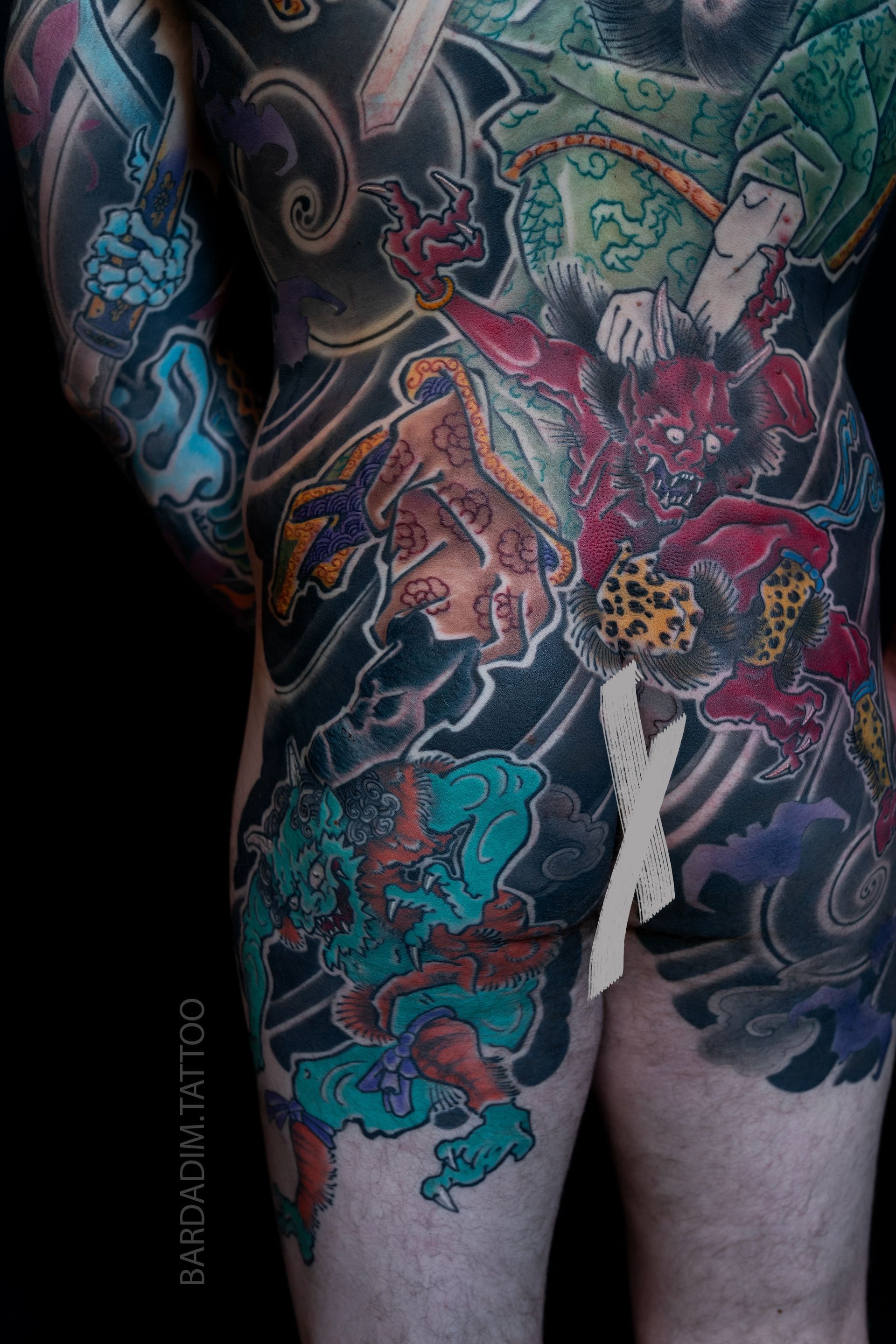 Full body tattoo of colorful Japanese demons and swirling clouds on a person's back.