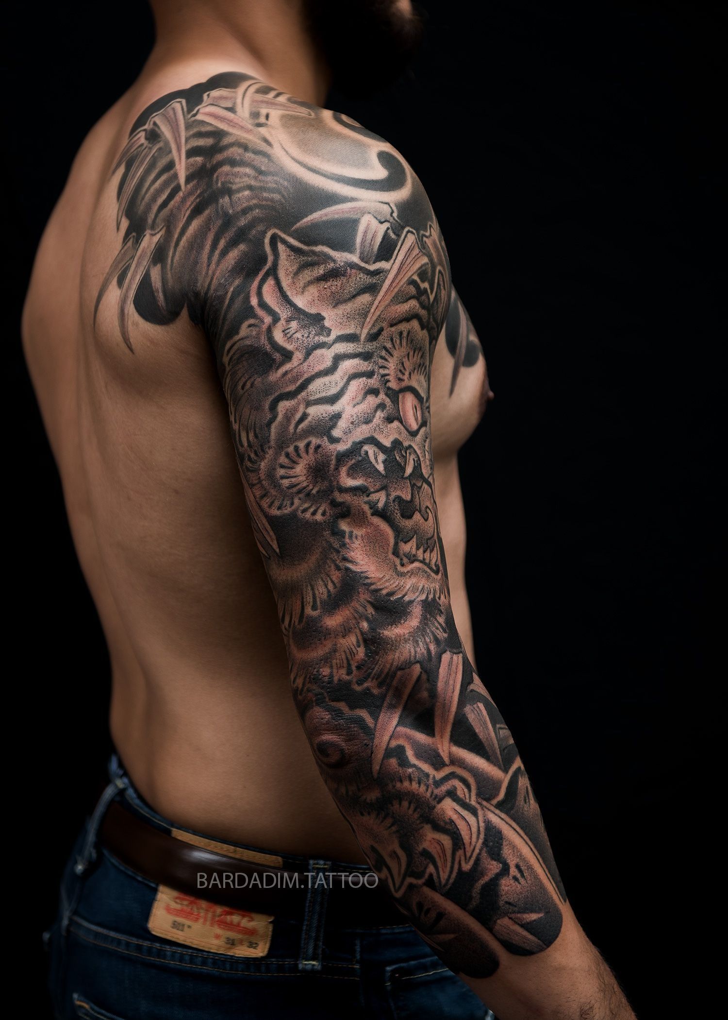 A shirtless man with a full sleeve tattoo on his arm.