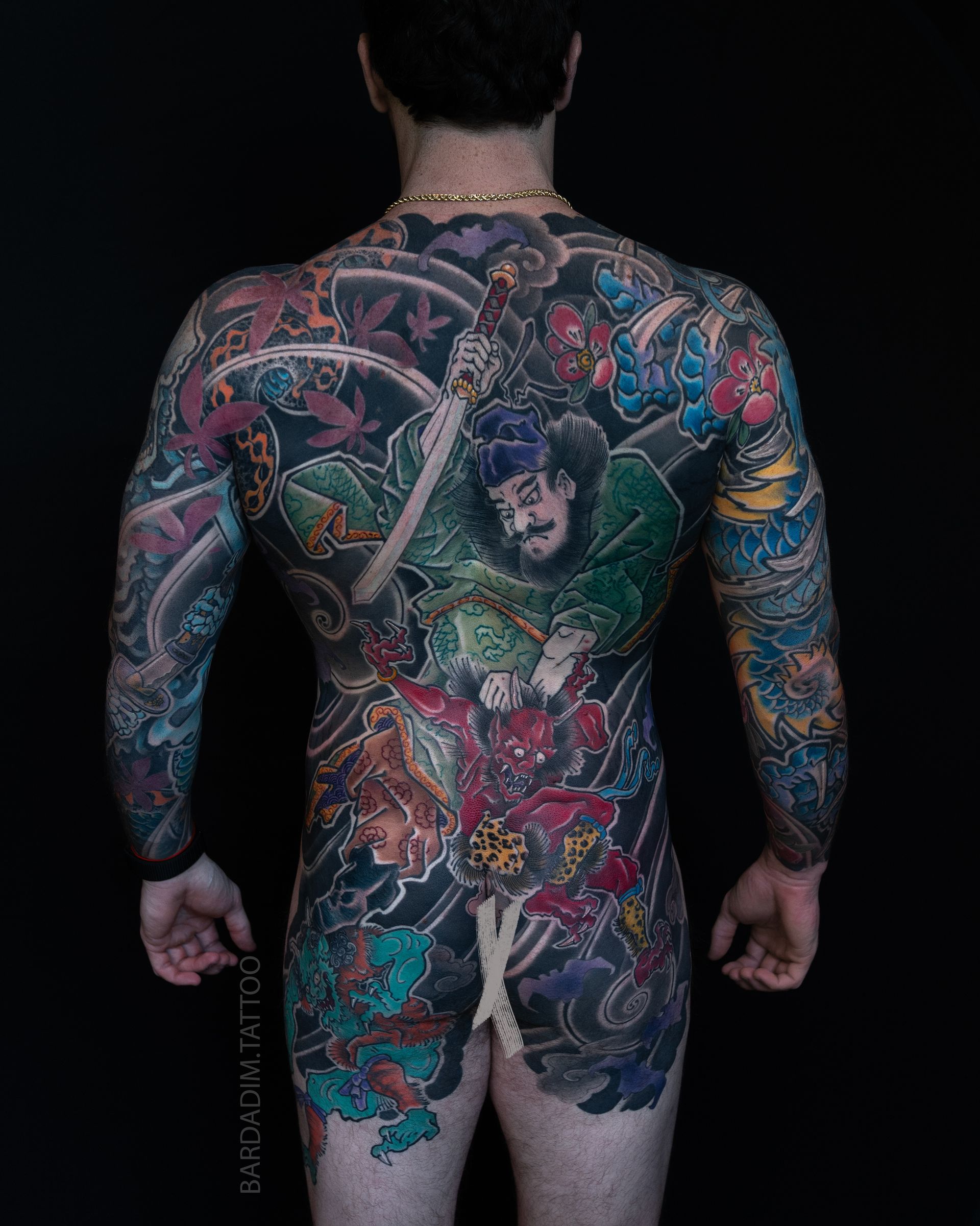 Full-body tattoo on person's back, a Japanese-style design featuring warriors, vibrant colors, and detailed patterns.