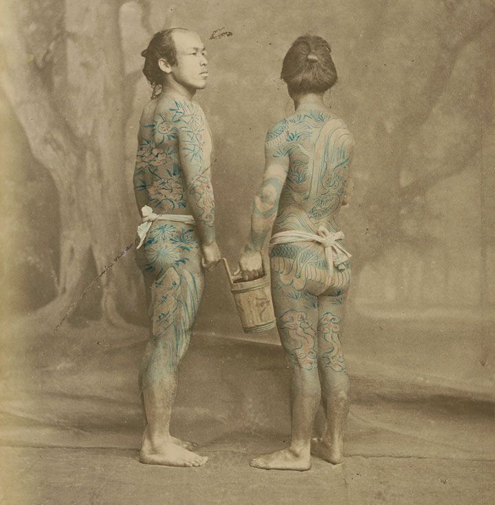Two men with tattoos on their bodies are standing next to each other.