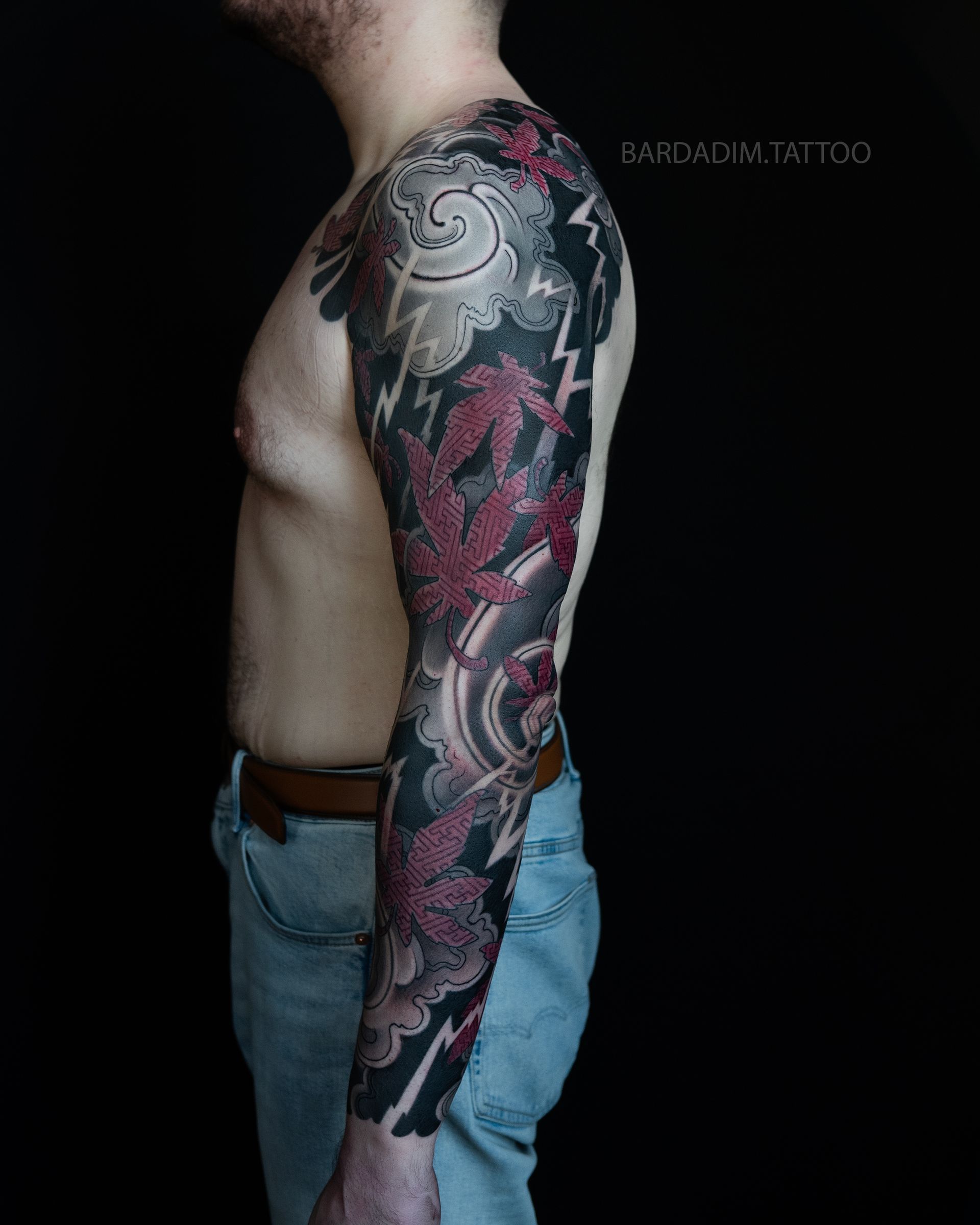 Side view of an irezumi full sleeve with red momiji maple leaves and lightning over dark storm clouds.