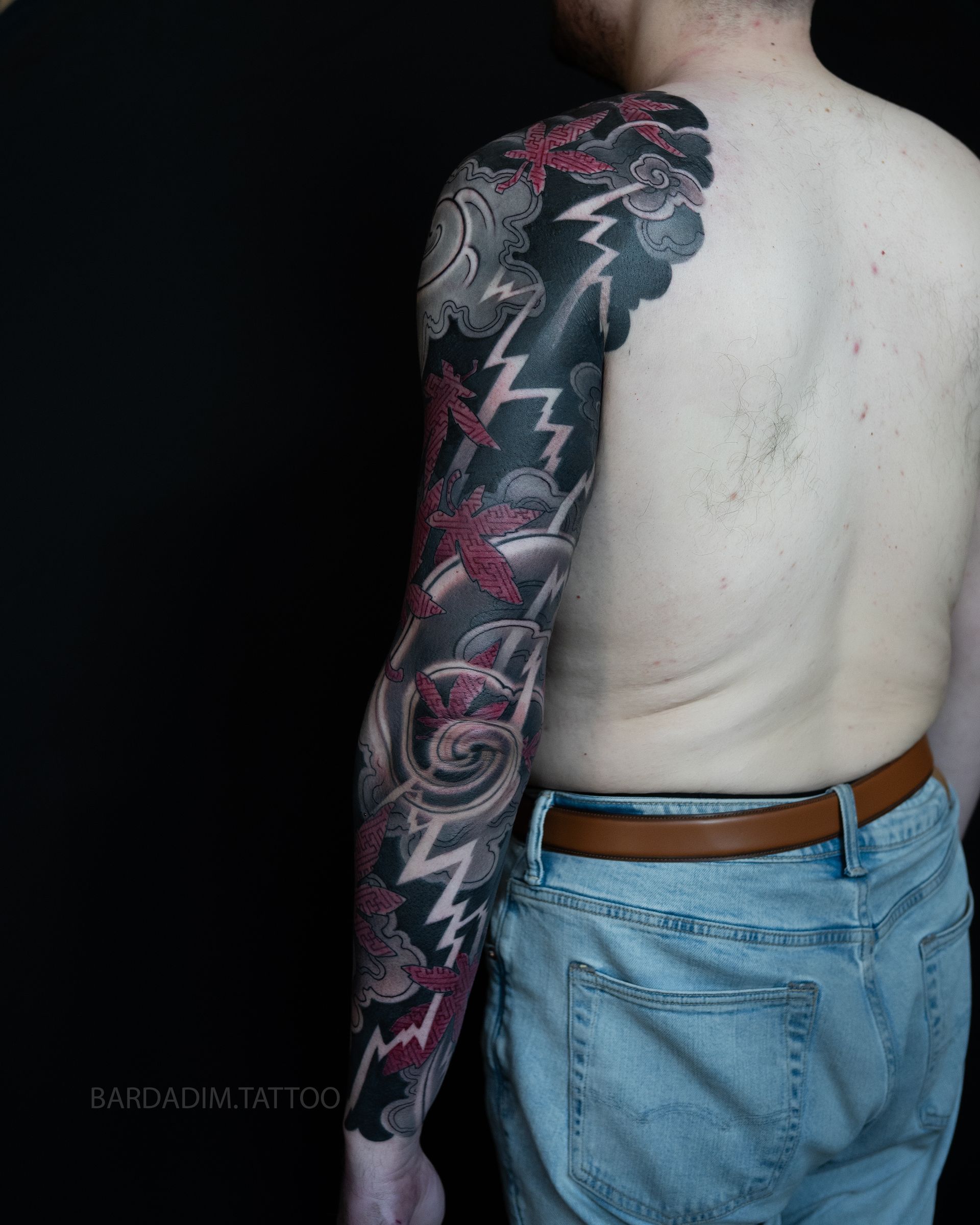 Outer-arm view of a maple leaf and storm cloud sleeve with lightning through a black ground.